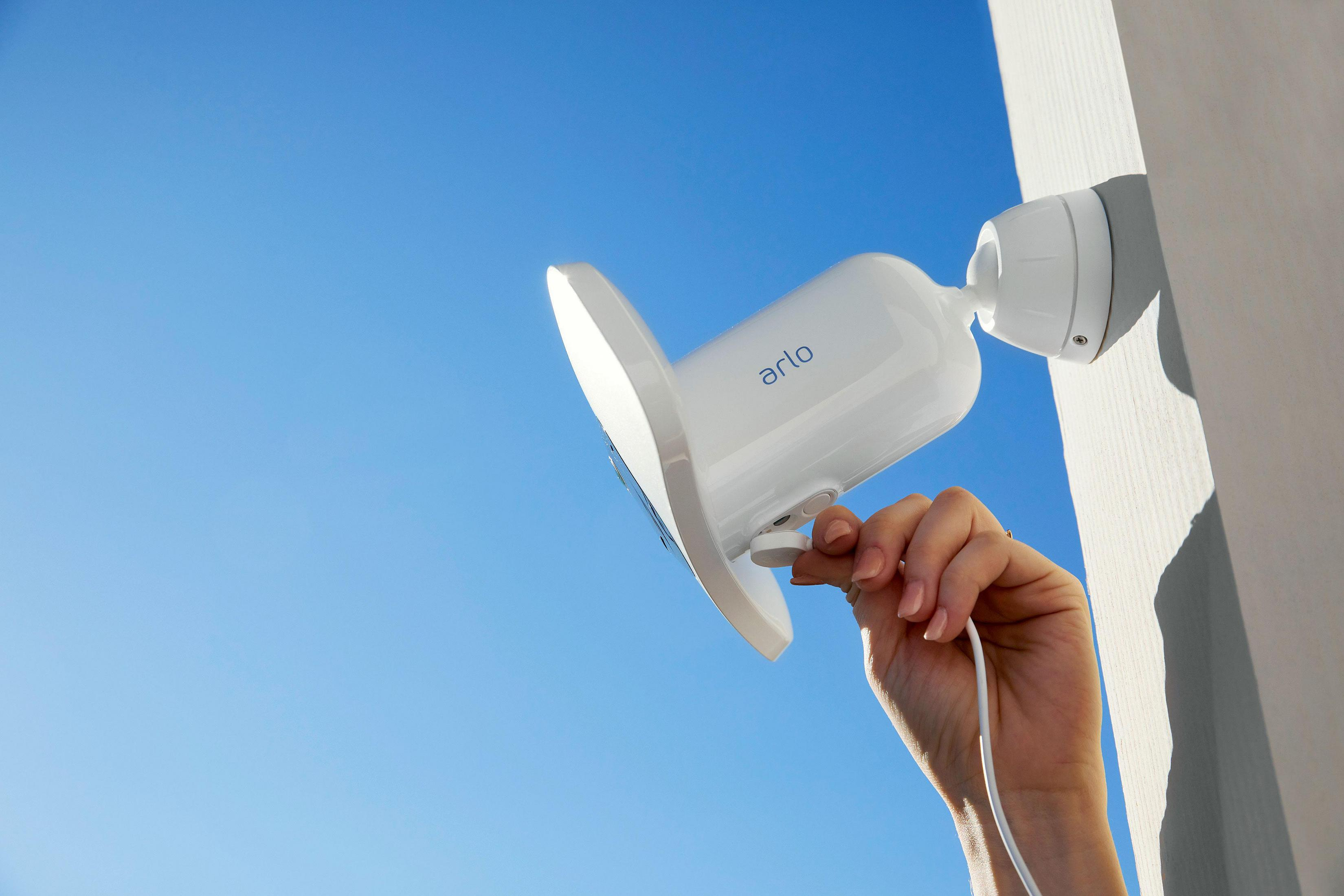 Biała kamera bezpieczeństwa przymocowana do ściany, z niebieskim niebem w tle.