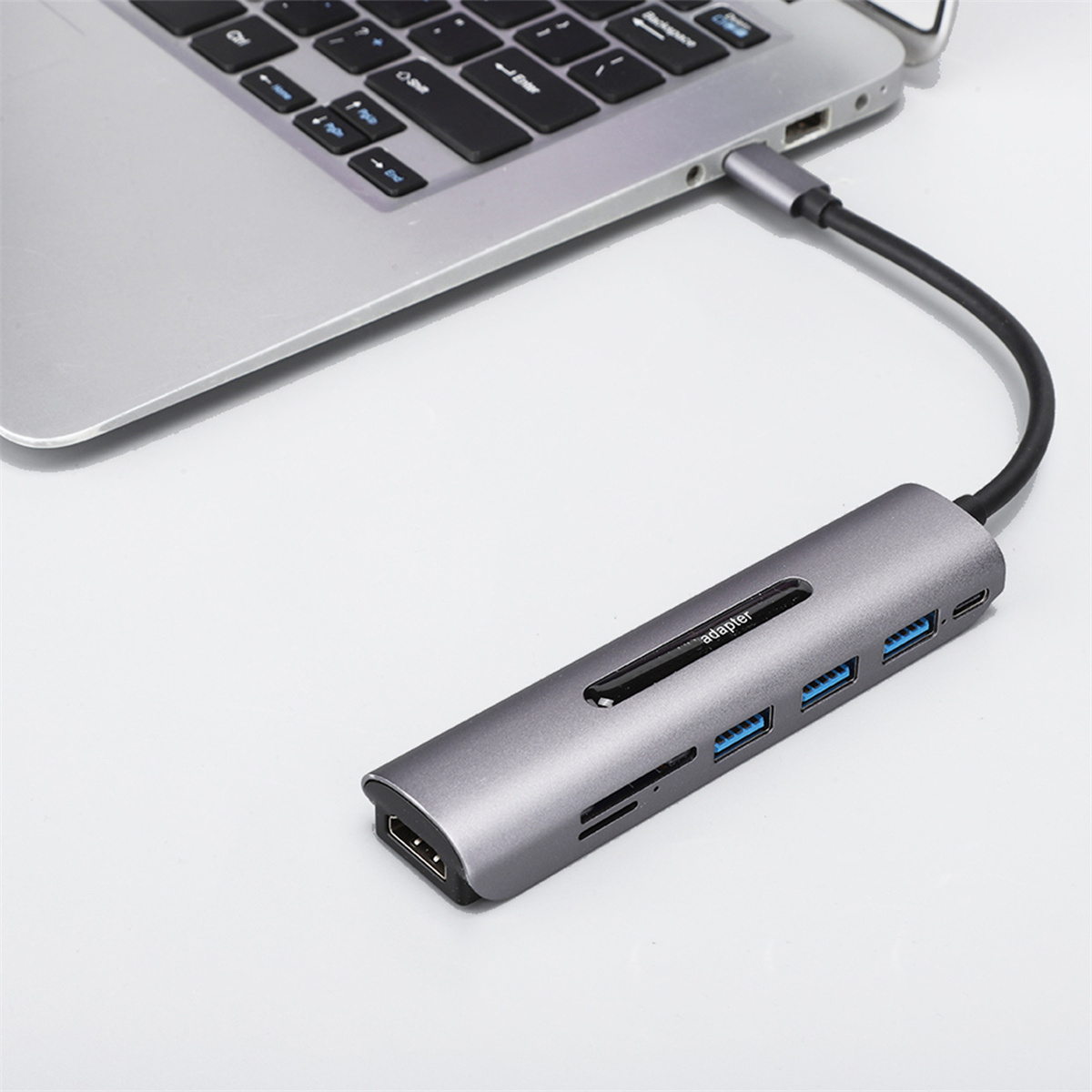 Grauer USB-C-Hub, an einen Laptop angeschlossen, mit mehreren Anschlüssen.