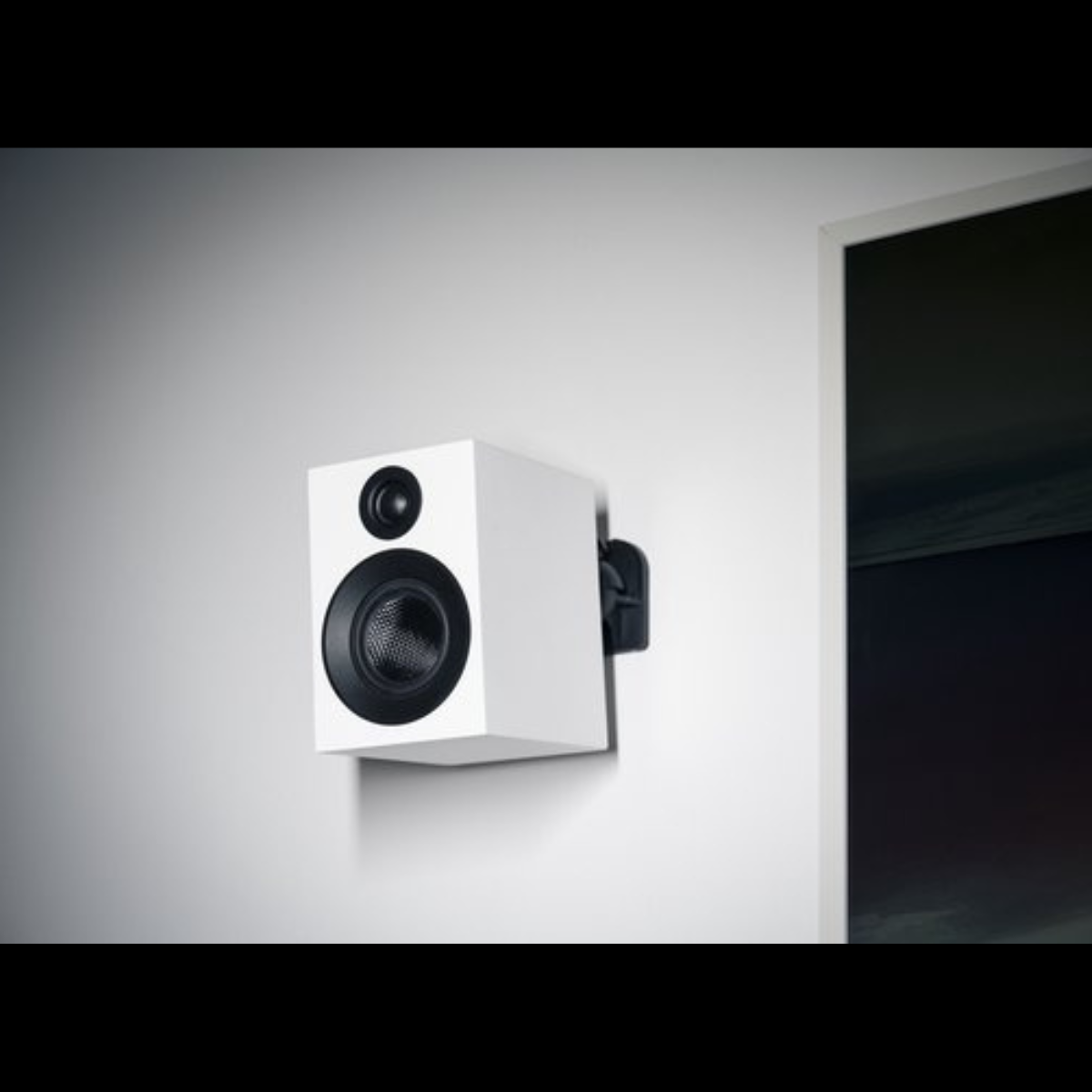 Biały głośnik zamontowany na ścianie, z czarnym głośnikiem i czarnym wspornikiem.