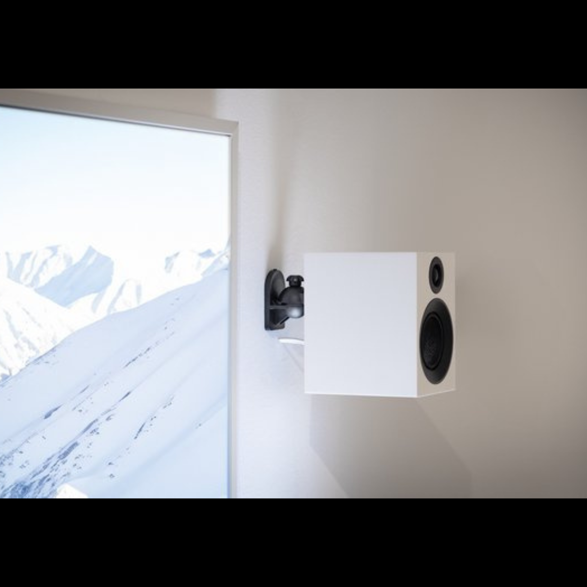 Biały głośnik zamontowany na ścianie, z widokiem na góry przez okno.