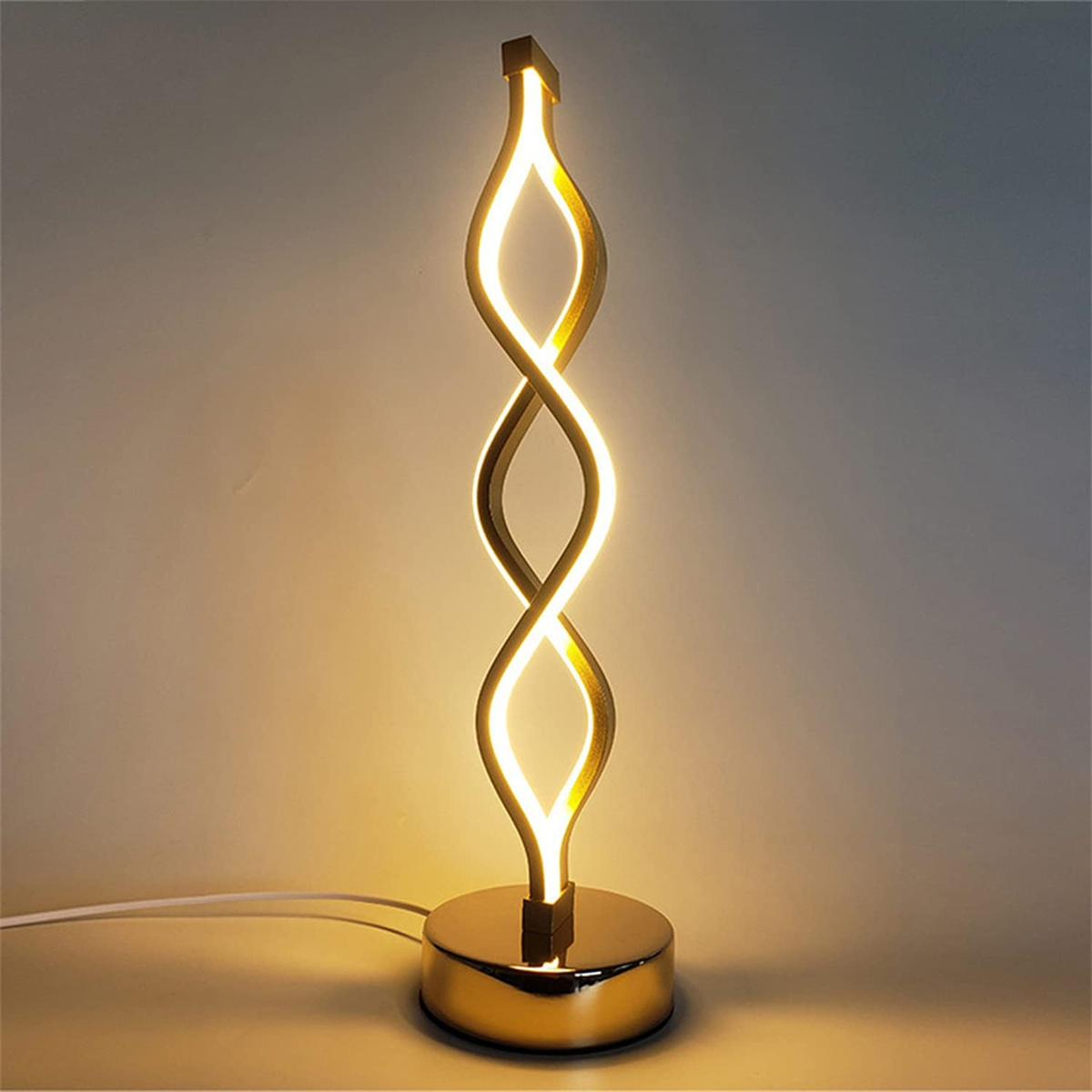 Goldfarbene Lampe. Sie hat ein spiralförmiges Design und einen runden Fuß. Das Licht scheint von der Lampe.