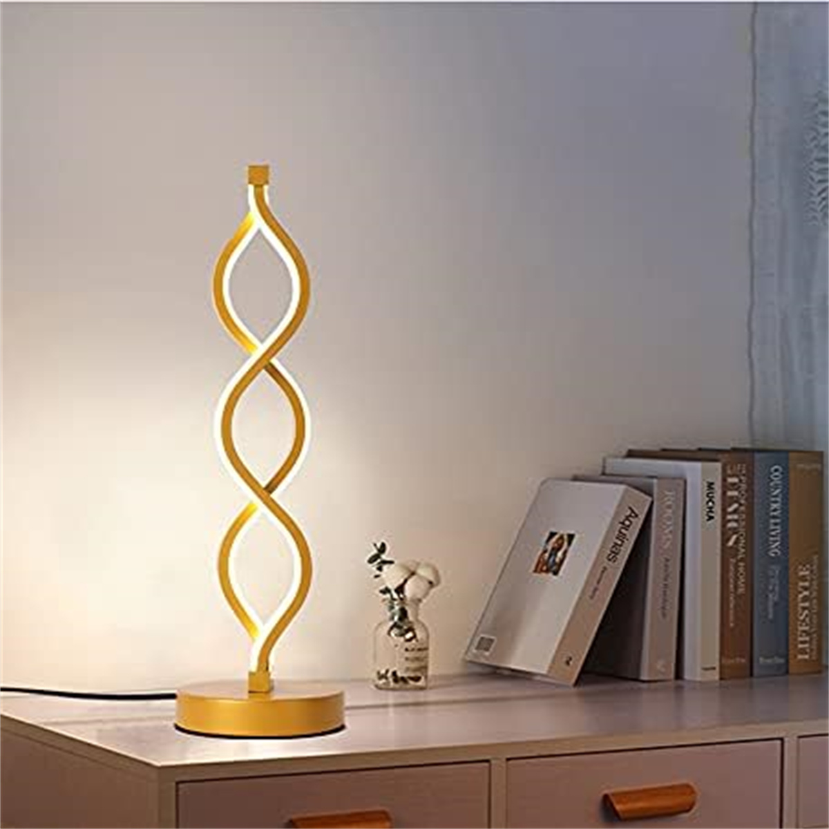 Eine gelbe Lampe mit geschwungenem Design auf einem Holztisch mit Büchern und einer Blumenvase.