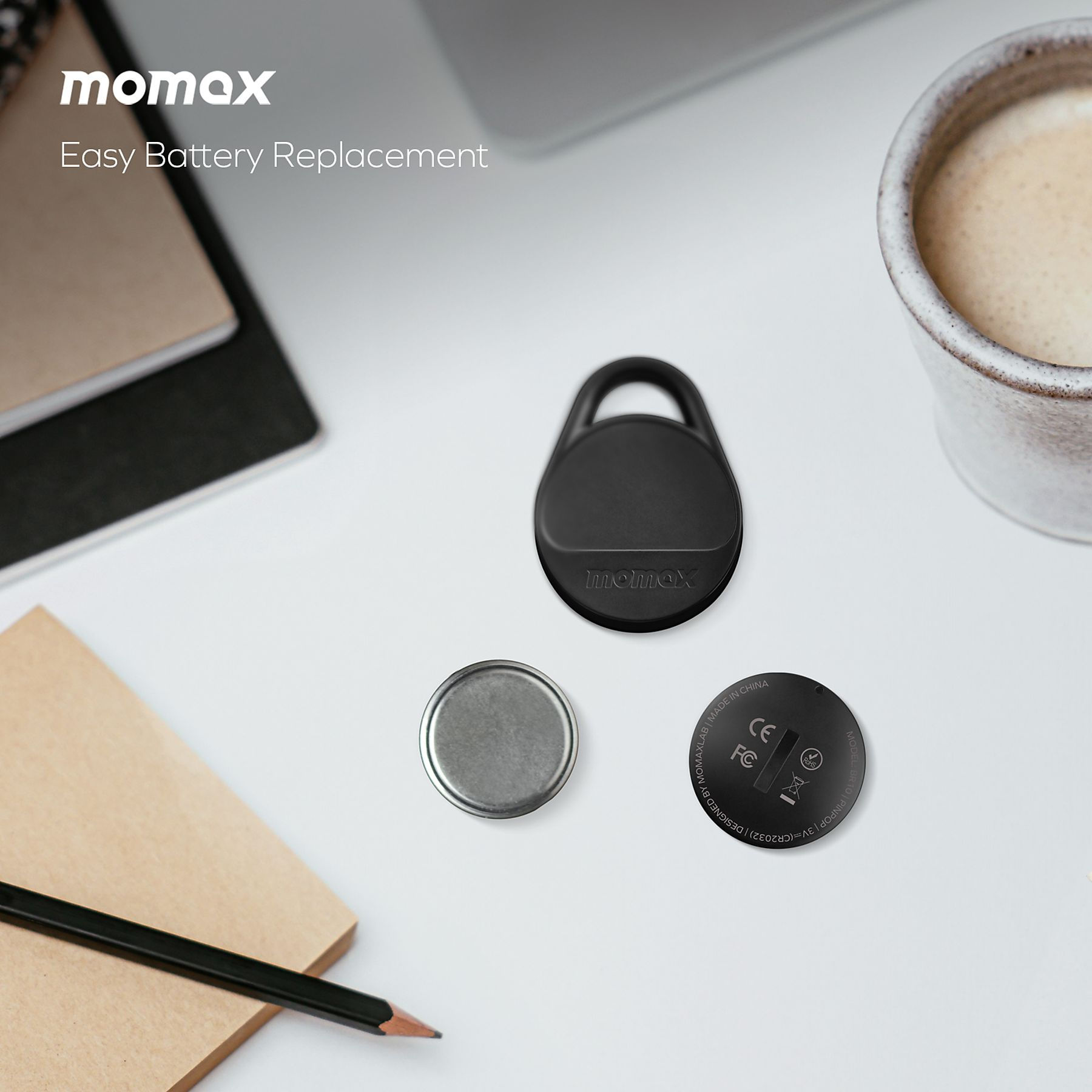 Black momax tracker, a battery, and another part on a white table with a pencil and a cup.
