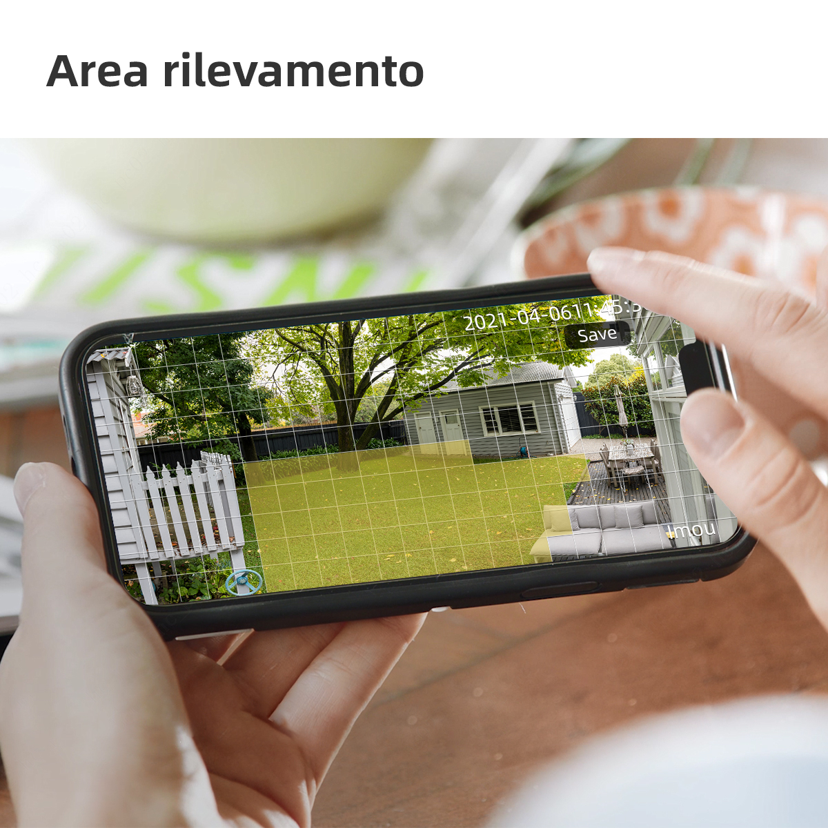 Eine Person hält ein Telefon, das einen Live-Kamera-Feed eines Hofes anzeigt, mit Rasterüberlagerung und Speichertaste.