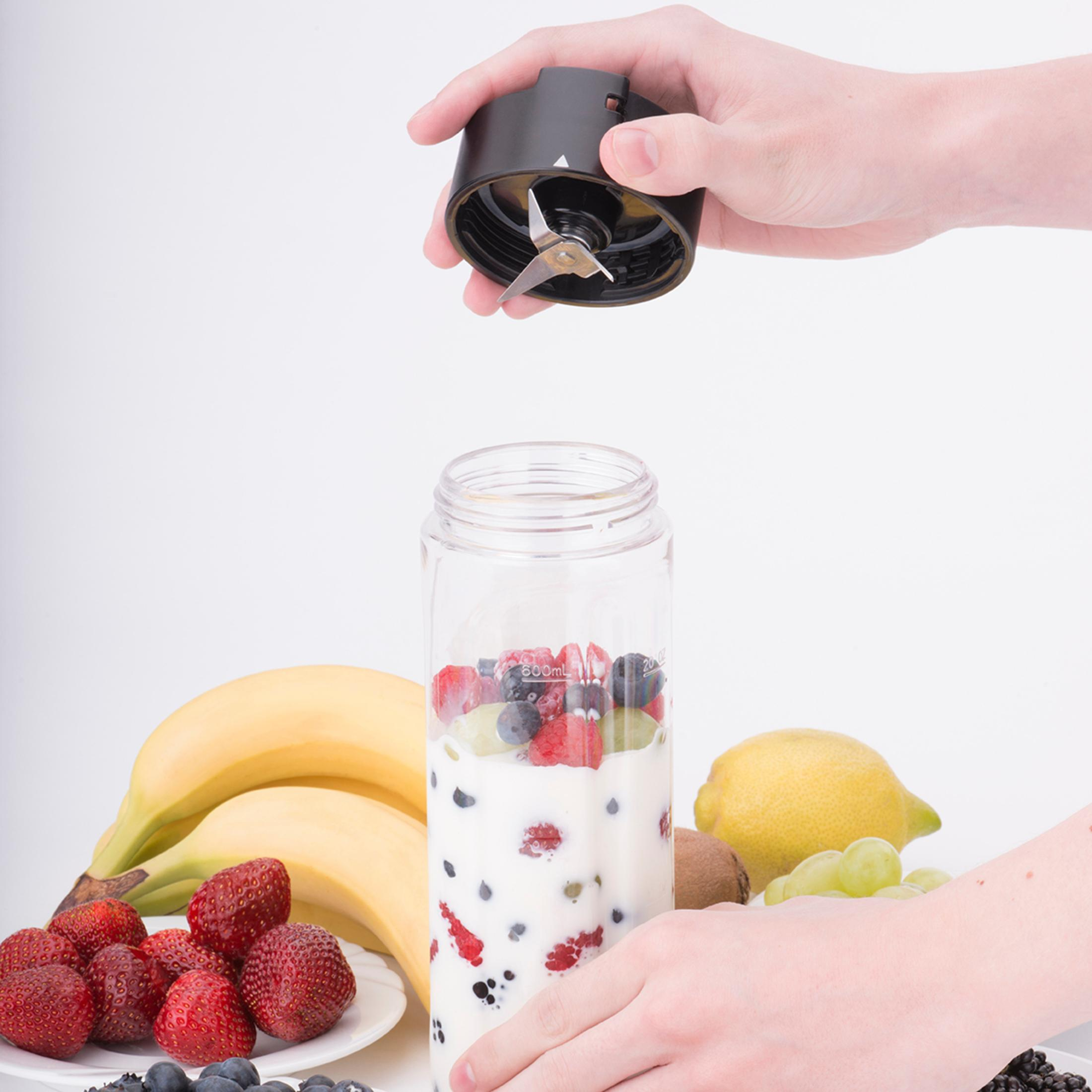 Eine Person hält eine schwarze Mixer-Klinge über einem transparenten Mixer-Glas, das mit Obst und Joghurt gefüllt ist.