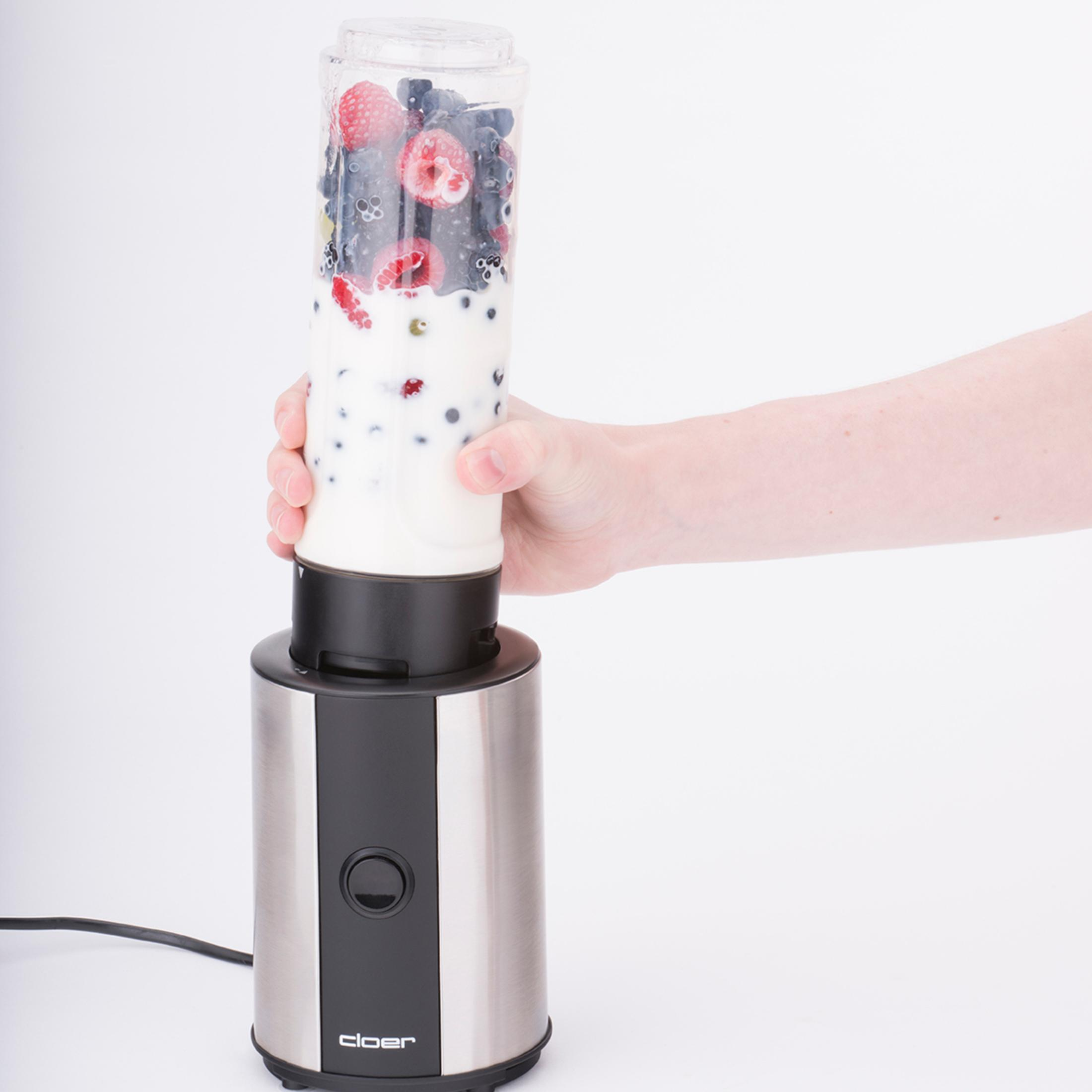 Hand hält einen Mixer mit Beeren und Milch, weißer Hintergrund.