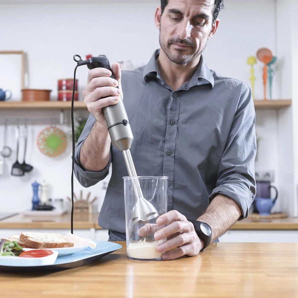 Mężczyzna blenduje srebrnym blenderem ręcznym w szklance.