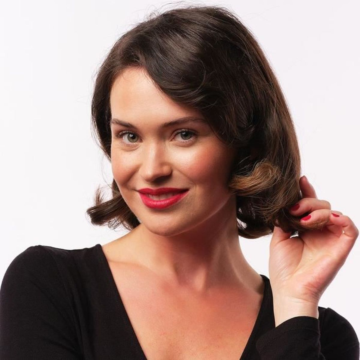 Frau mit dunklem Haar, rotem Lippenstift, lächelnd, hält ihr Haar.