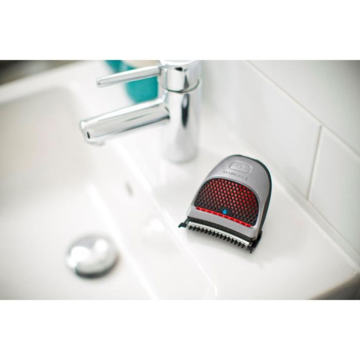 Srebrna golarka elektryczna na białej umywalce, z czerwonymi detalami, zbliżenie.