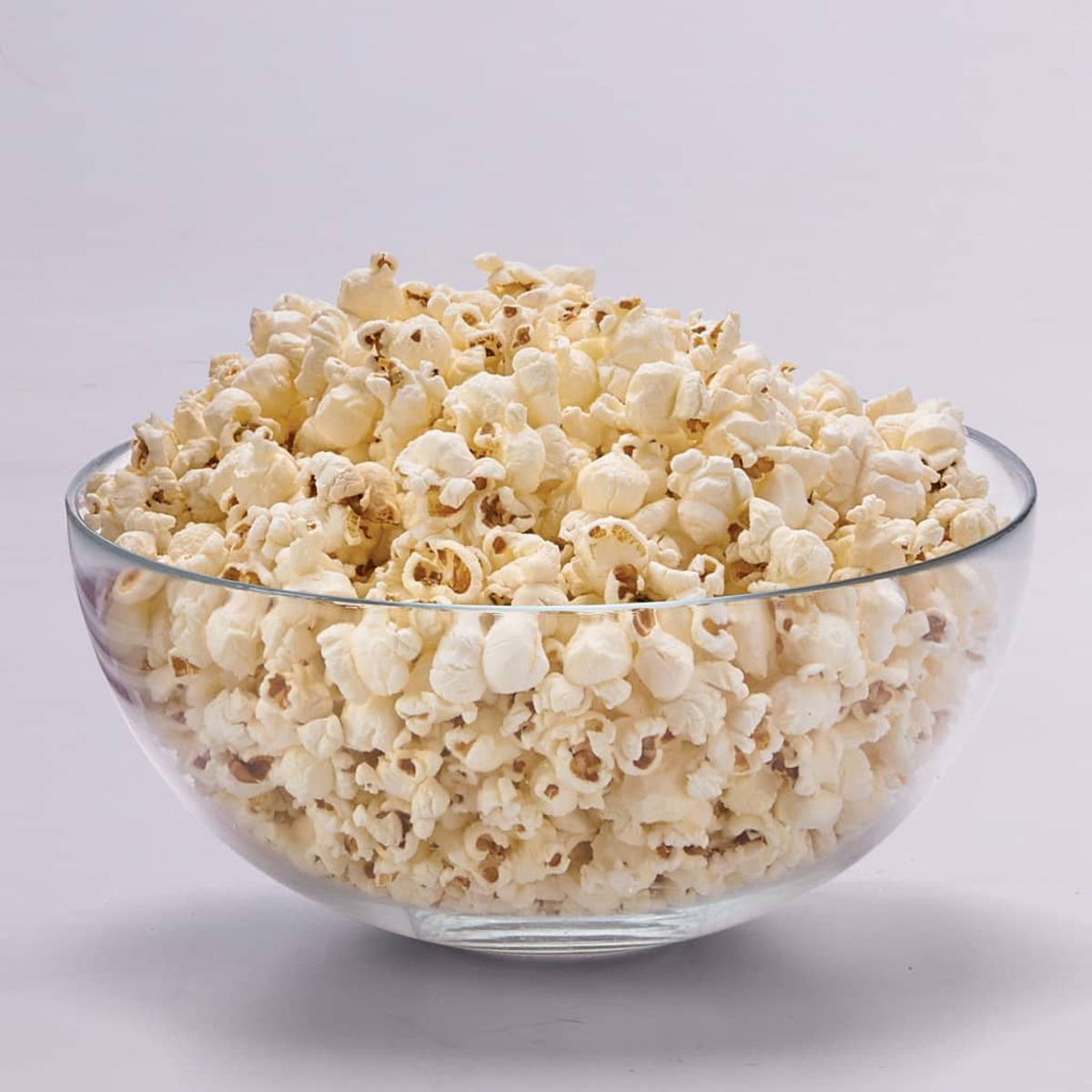 Una ciotola di vetro piena di popcorn su sfondo bianco.