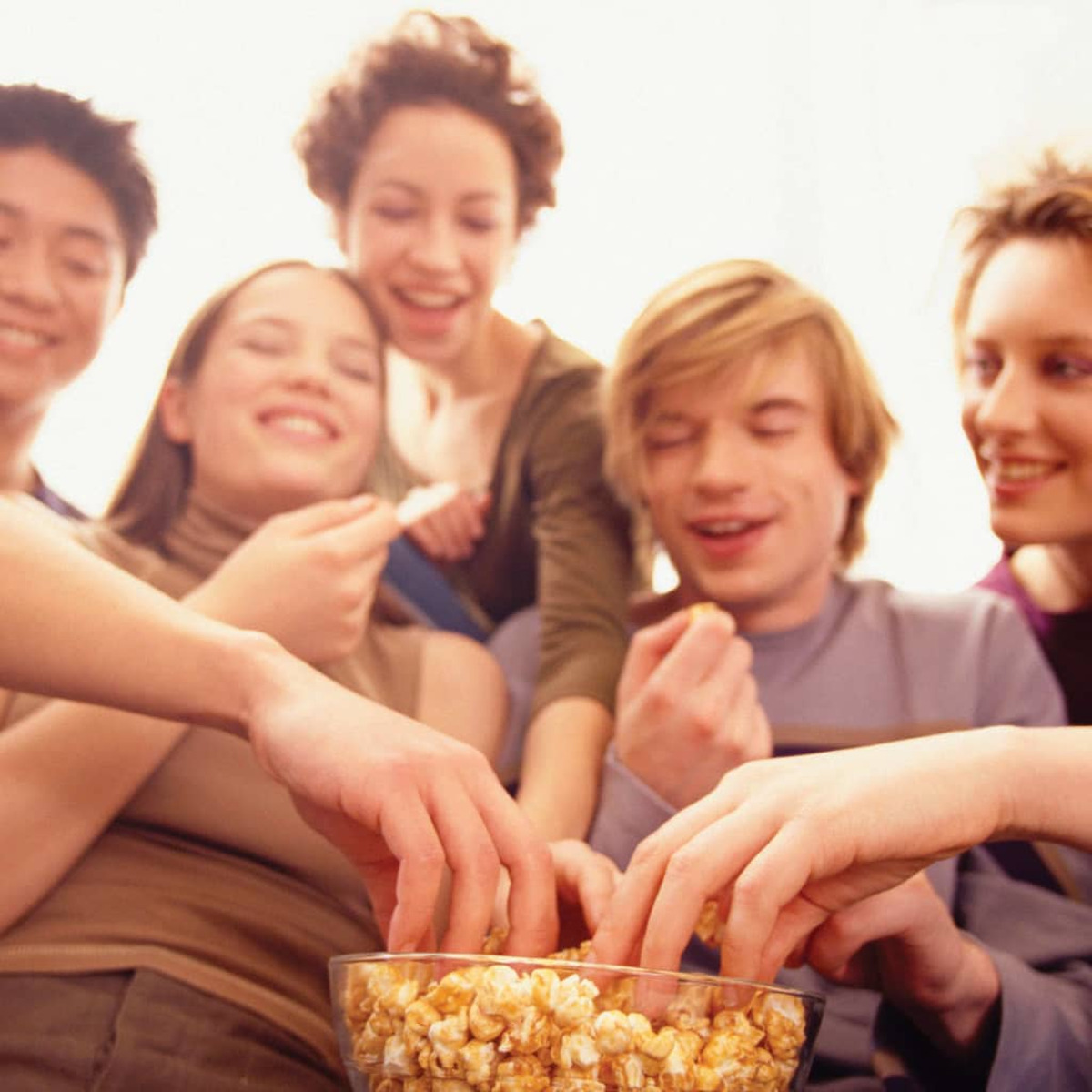 Gruppo di persone che condividono popcorn da una ciotola. Sorridono e si godono il cibo.