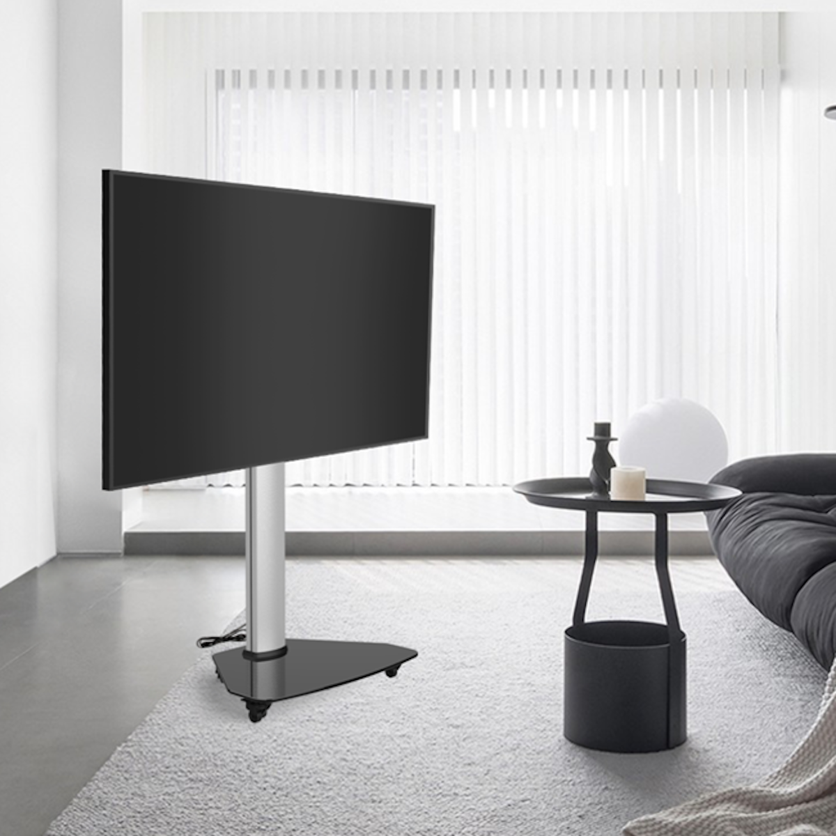 Une grande télévision noire sur un support. Une petite table avec déco et un canapé sont présents.