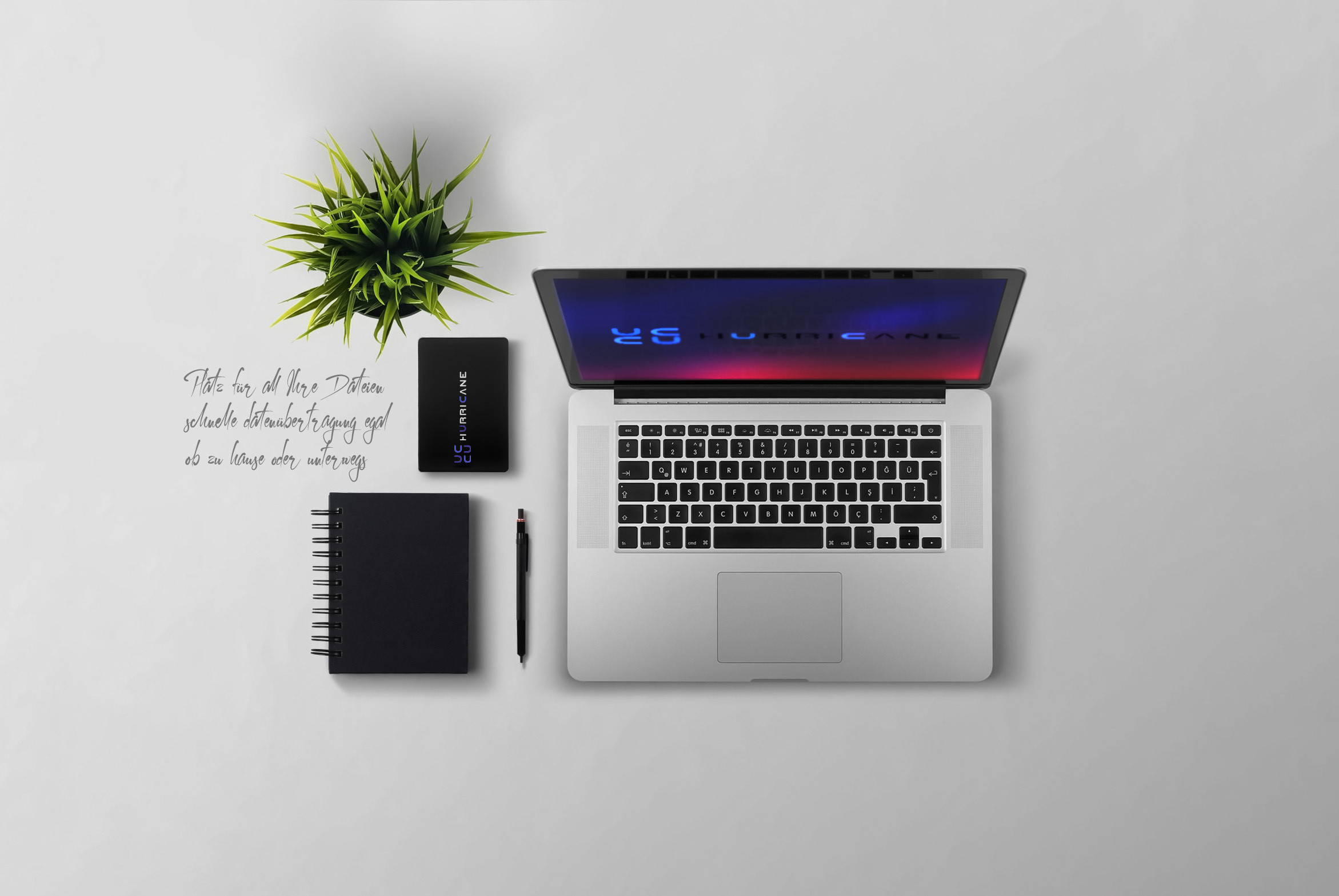 Laptop, Notizbuch und externe Festplatte auf weißer Oberfläche mit kleiner Pflanze und Stift.