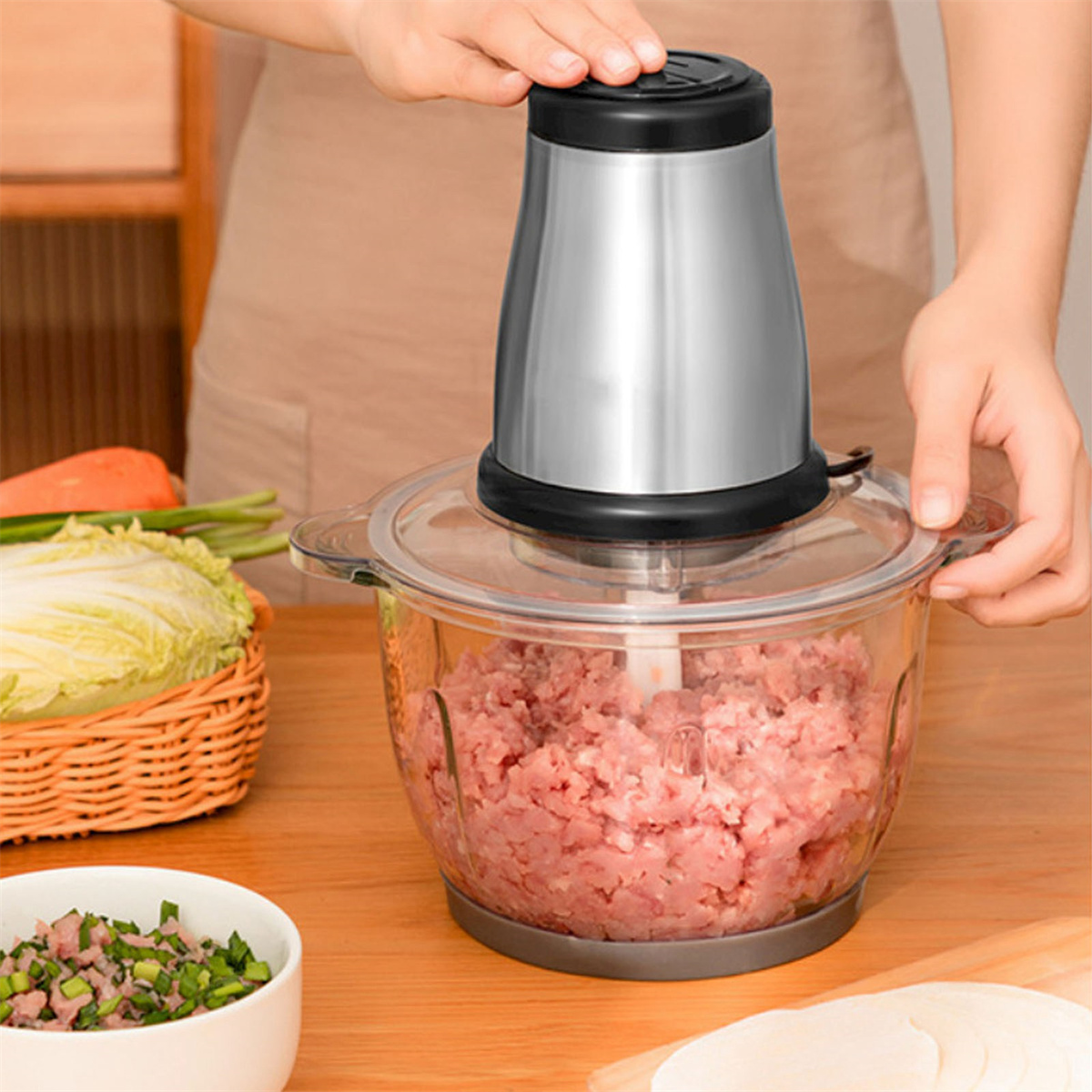 Eine Person verwendet einen silbernen Foodprozessor mit Hackfleisch, neben Kohl und Grünzeug.