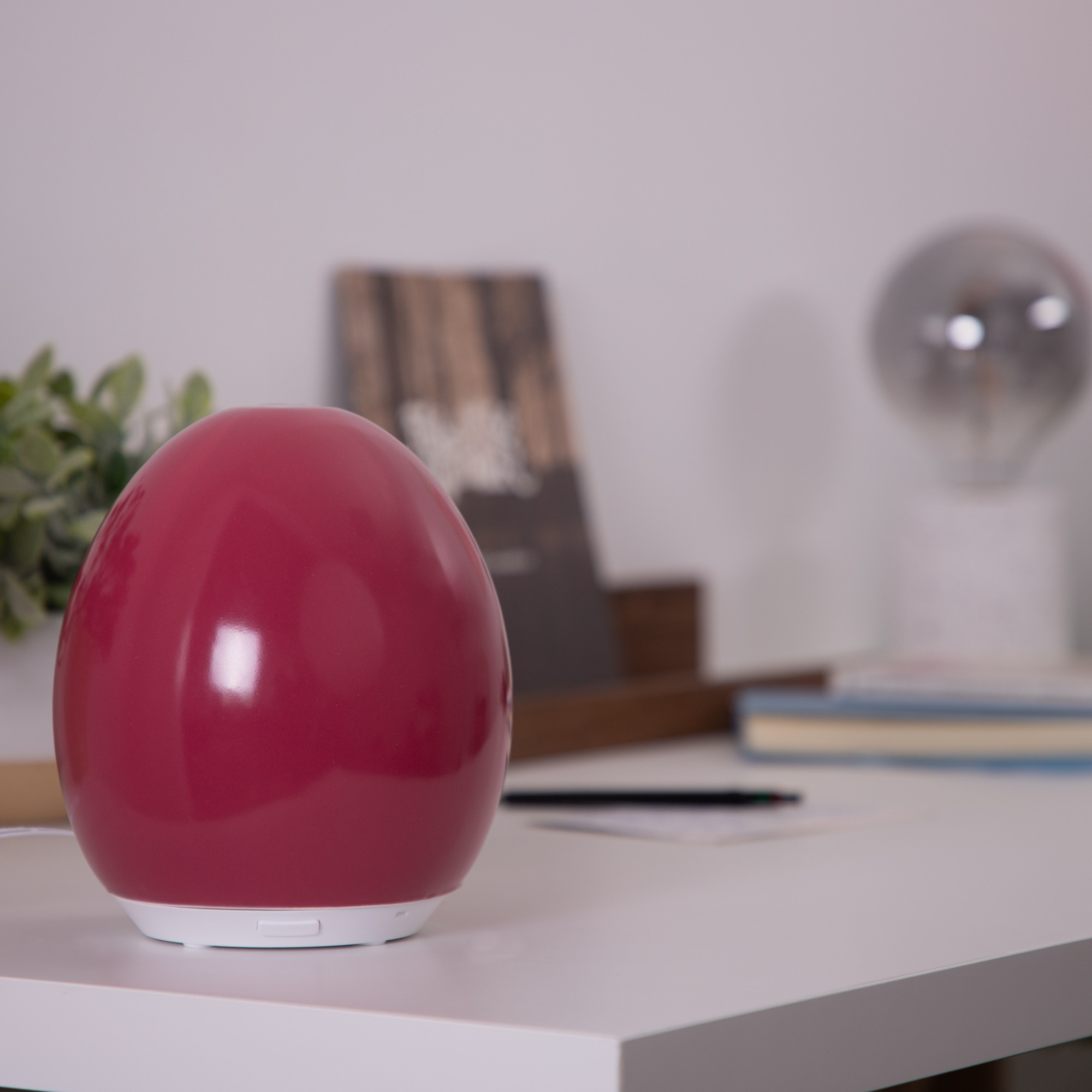 A red egg-shaped diffuser on a white surface, desk setting.
