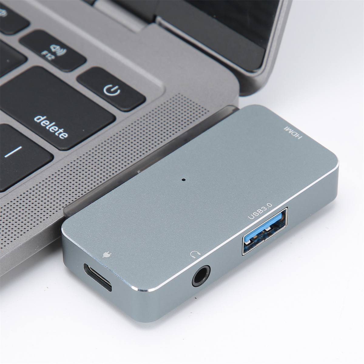 Ein grauer USB-Hub, der mit einem Laptop verbunden ist. Er hat Anschlüsse für HDMI, USB 3.0 und Audio.