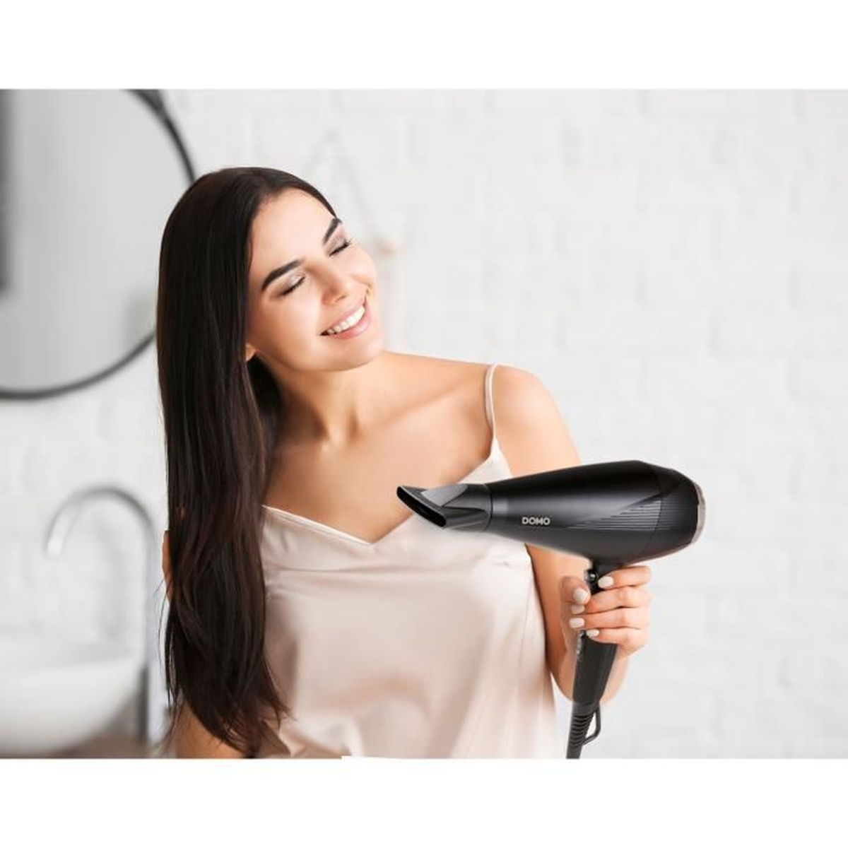 Una donna con lunghi capelli scuri sorride mentre tiene in mano un asciugacapelli nero.