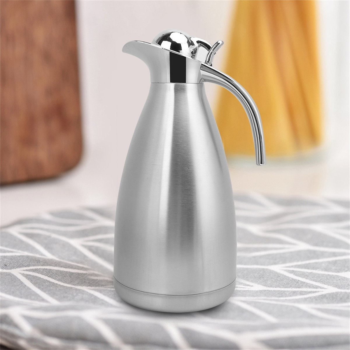 Glänzende silberne Thermokaraffe mit Griff auf einer grauen, gemusterten Oberfläche.