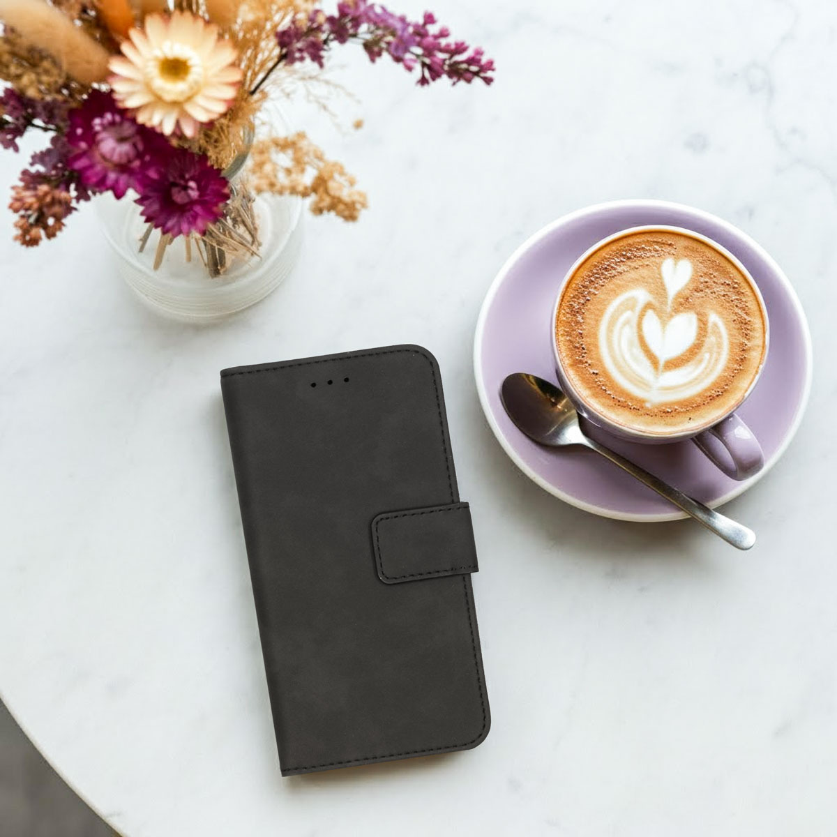 Une table avec un café, des fleurs et un étui de téléphone noir fermé.