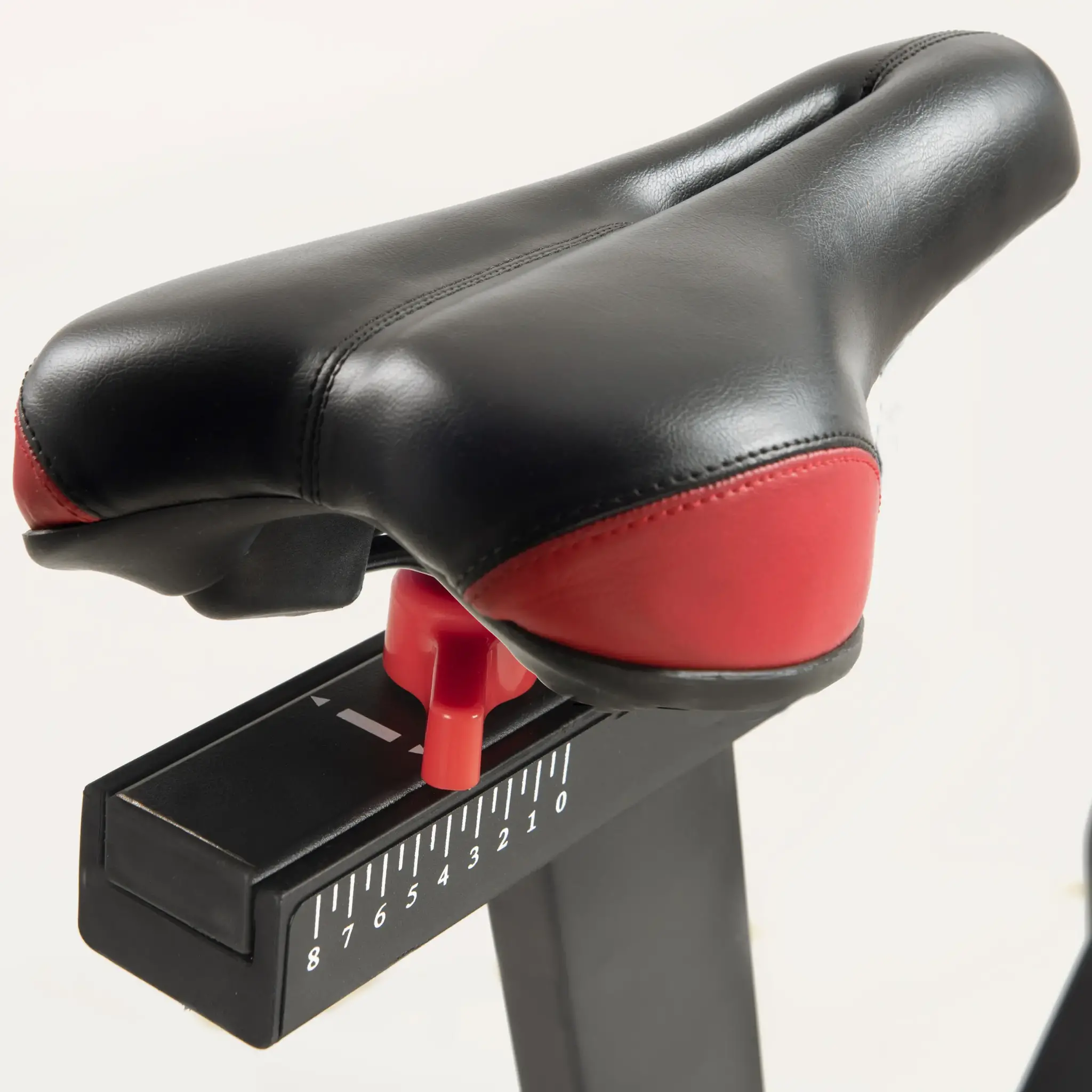 Een fietszadel, zwart met rode accenten, verstelbaar met een rode knop en een genummerde schaal.