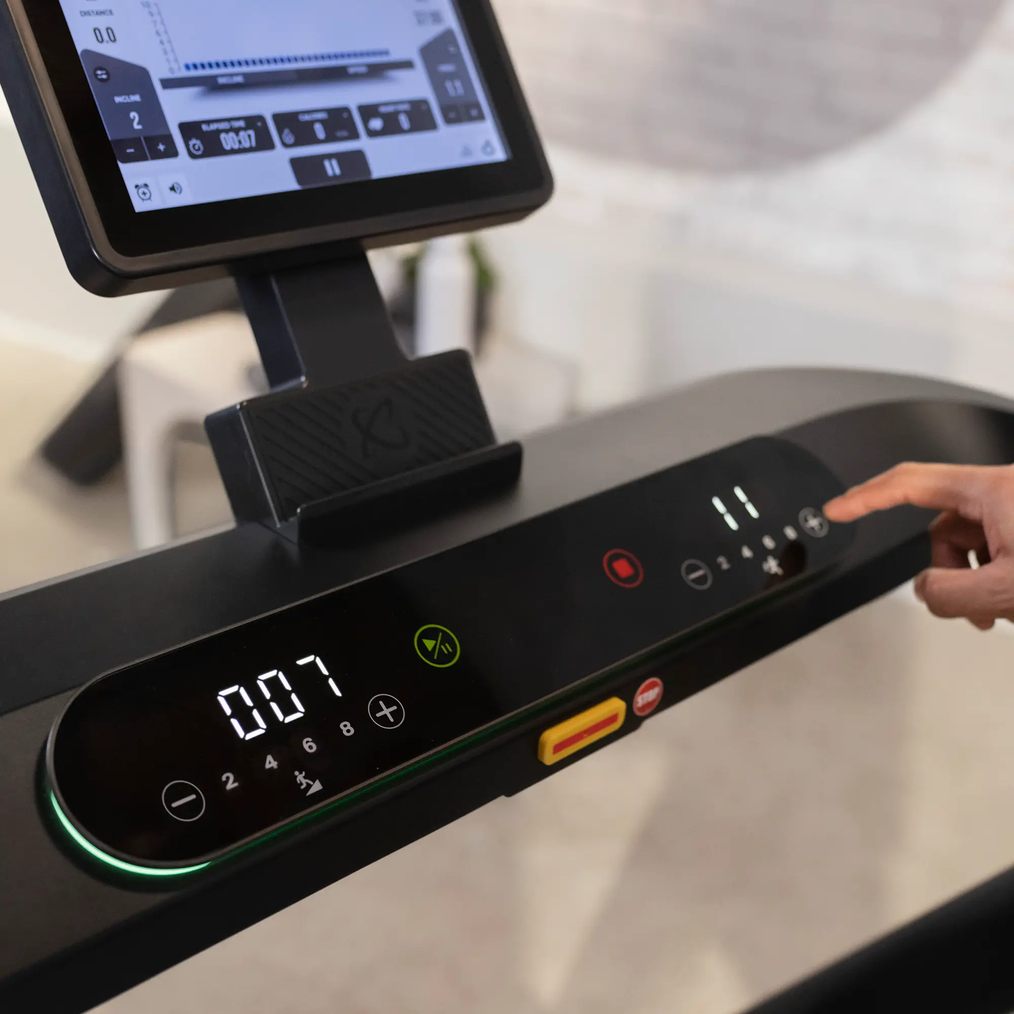 Close-up of a treadmill console, displaying numbers, and a hand pressing buttons.