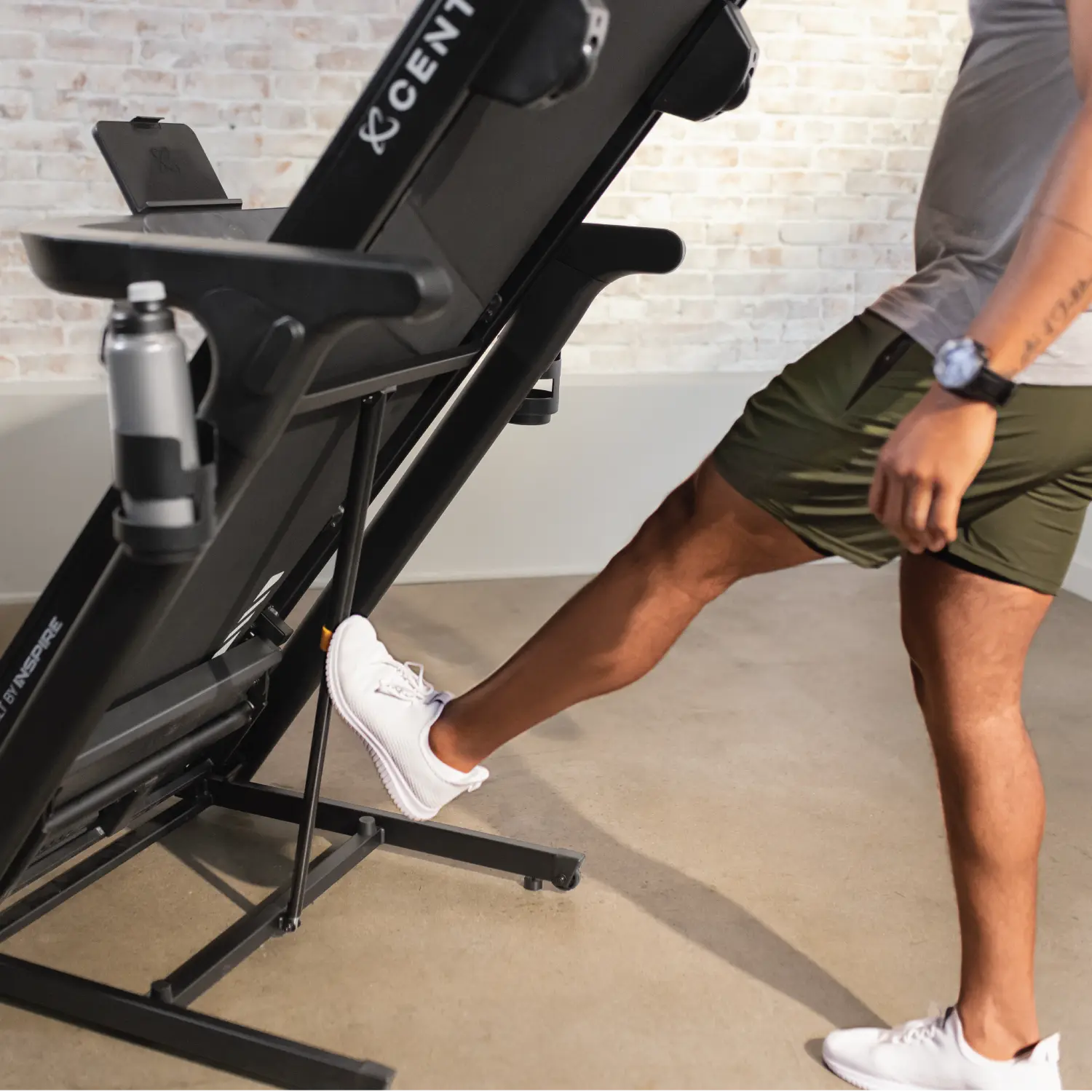 A person wearing white shoes is stepping on a treadmill with a water bottle.