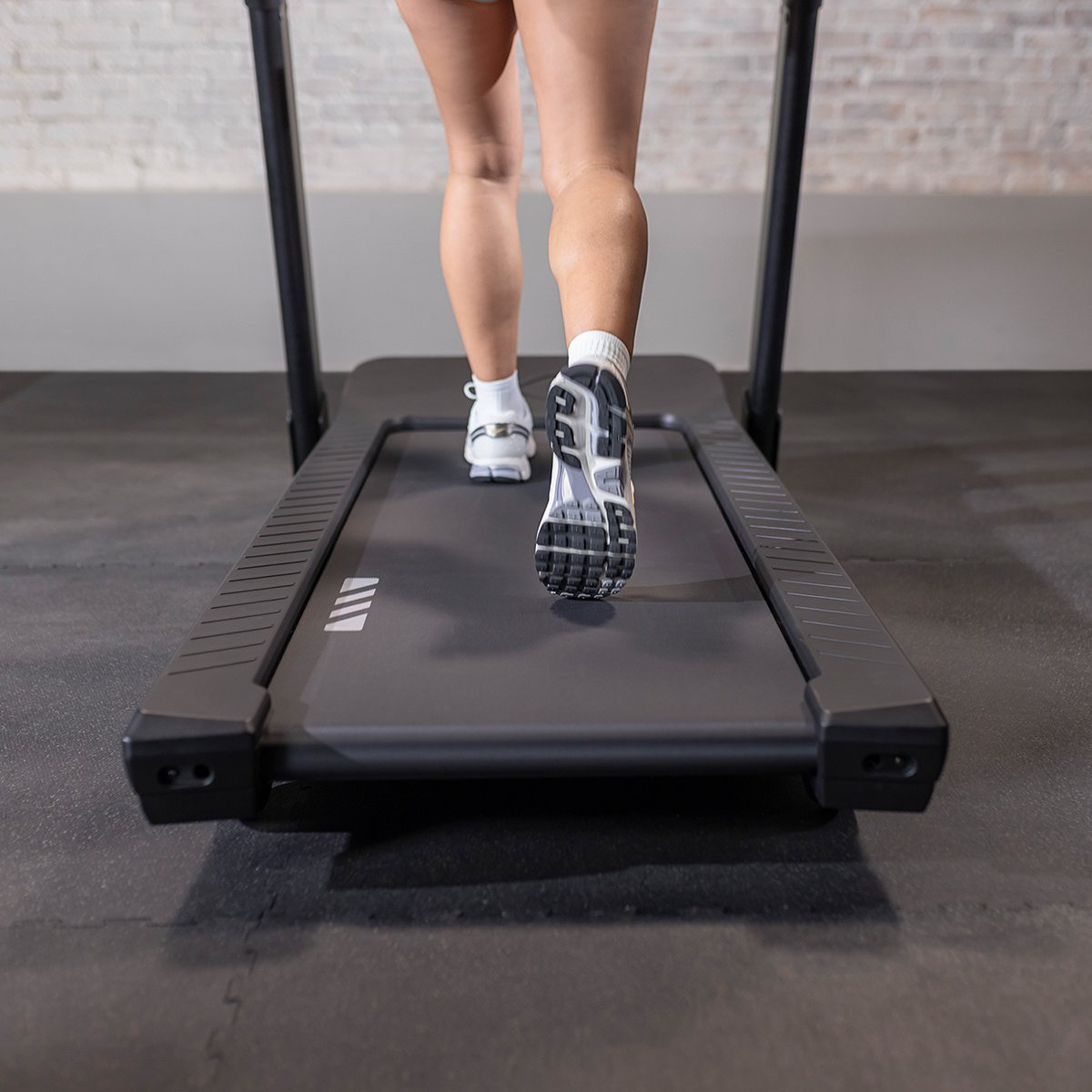 A person running on a black treadmill. The person is wearing running shoes.