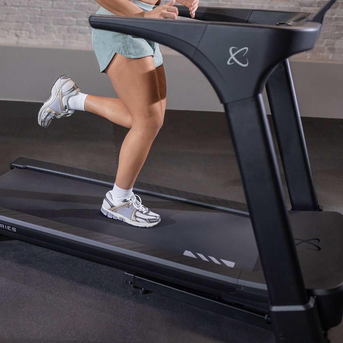 A person running on a treadmill. They wear white shoes and gray shorts. The machine is black.