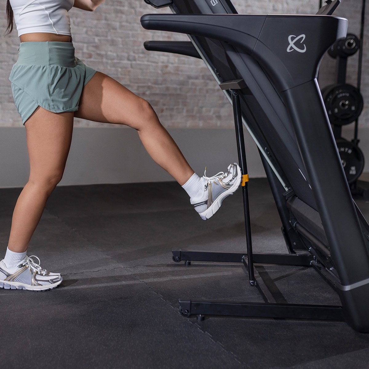 Woman running on a treadmill. Her left leg is raised and she is about to step forward.