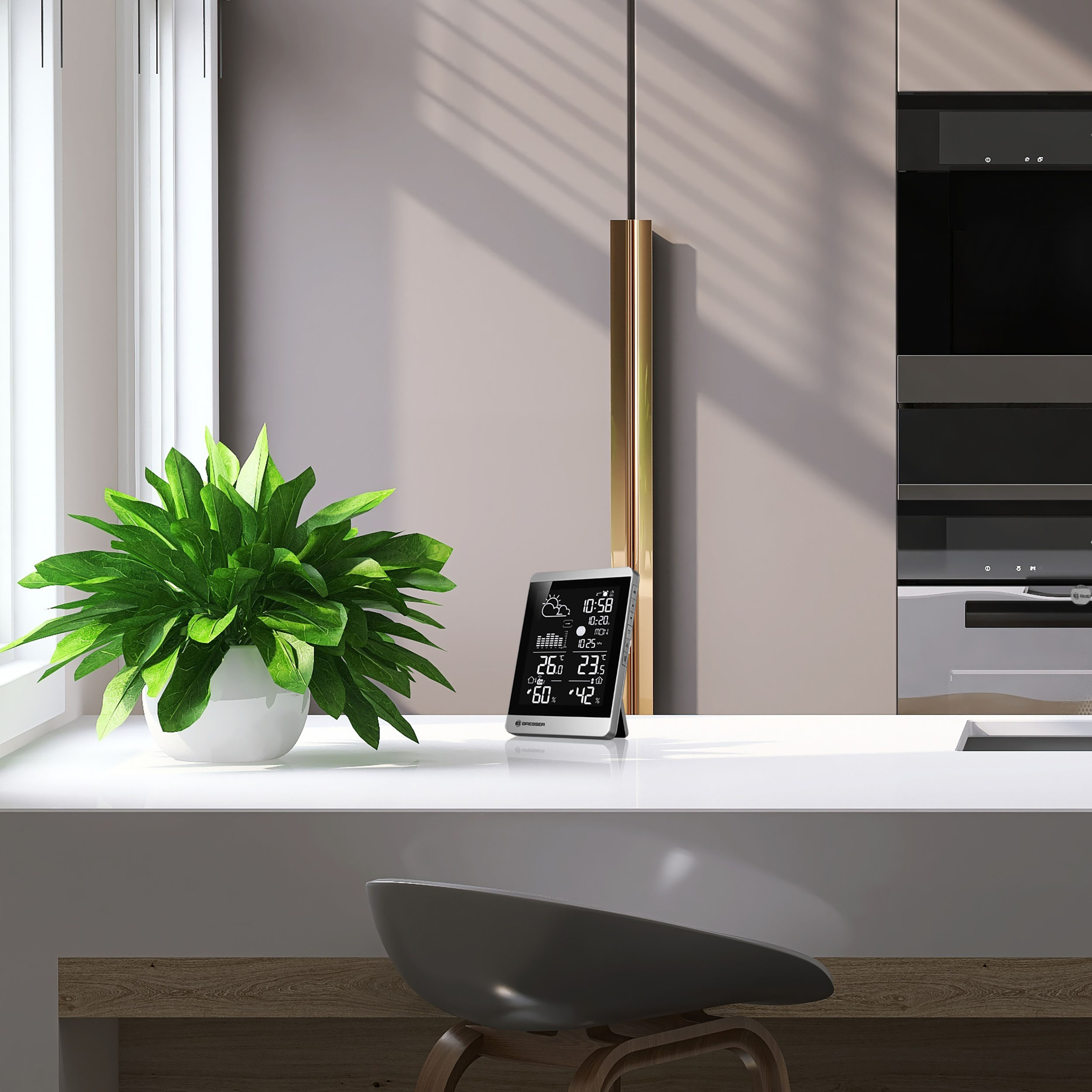 Una encimera blanca con una planta y una estación meteorológica digital con una silla gris.