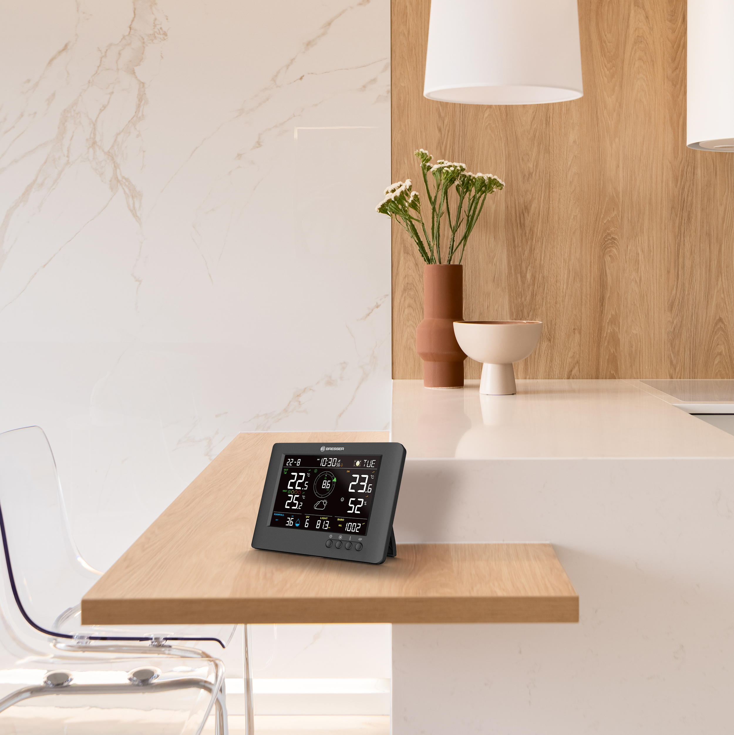 Una estación meteorológica digital está en una encimera de madera en una cocina.