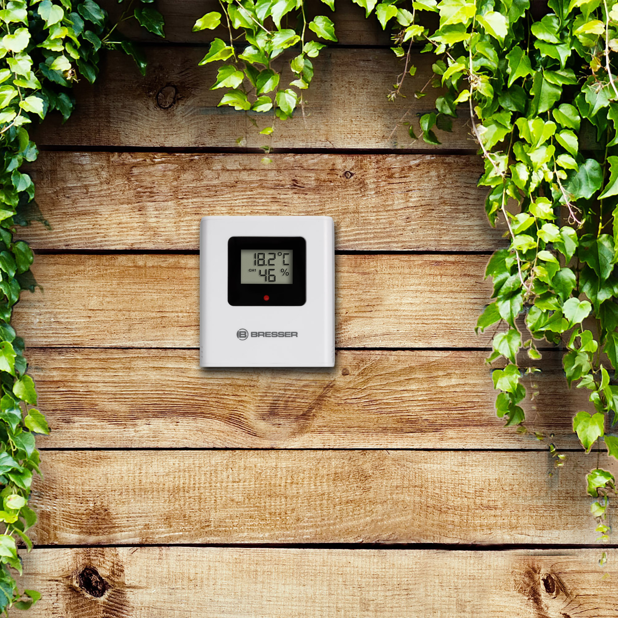 Un termómetro digital blanco en una pared de madera, mostrando lecturas de temperatura y humedad.
