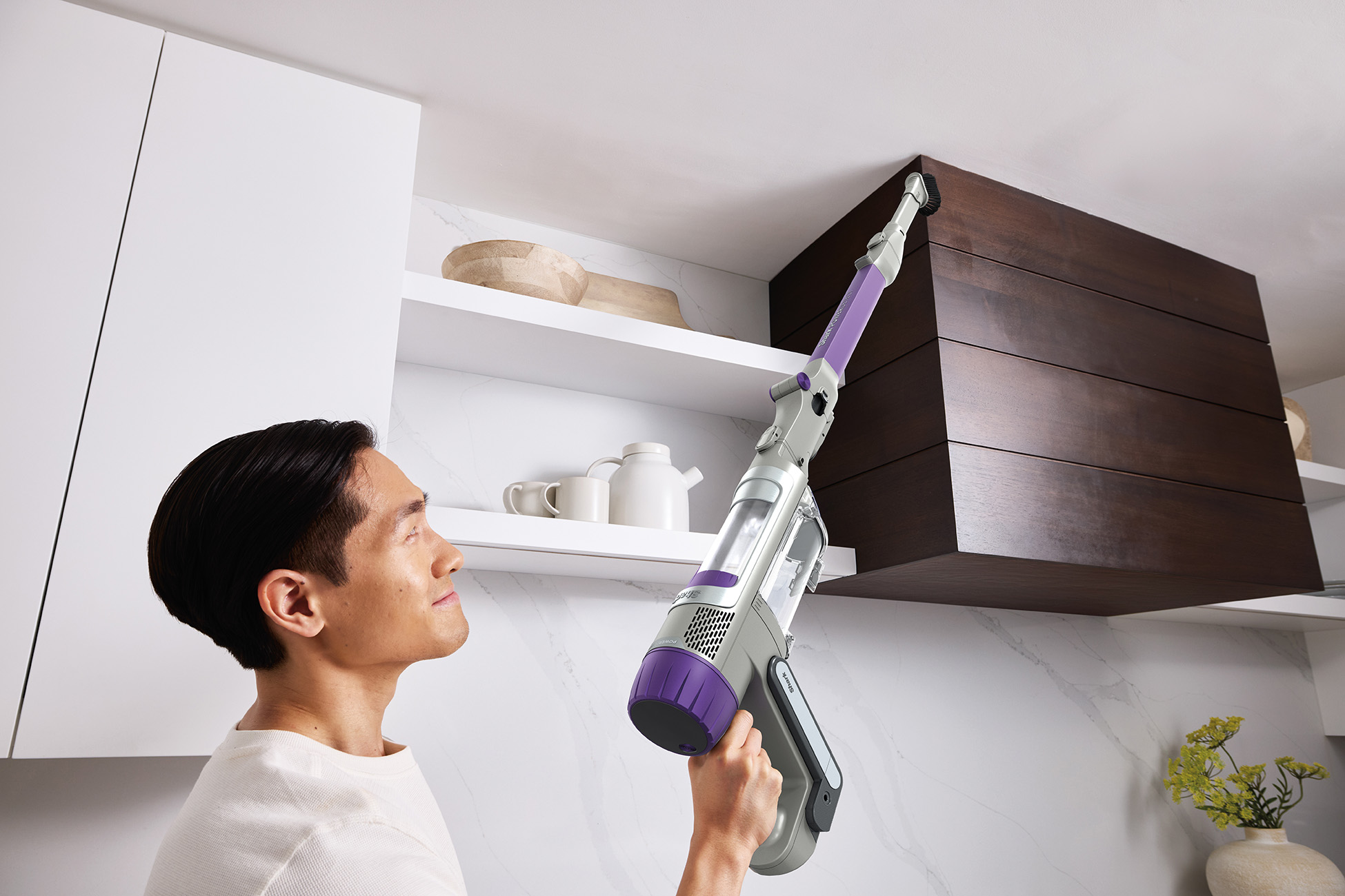 Man vacuums a kitchen ceiling vent with a purple and gray cordless vacuum cleaner.