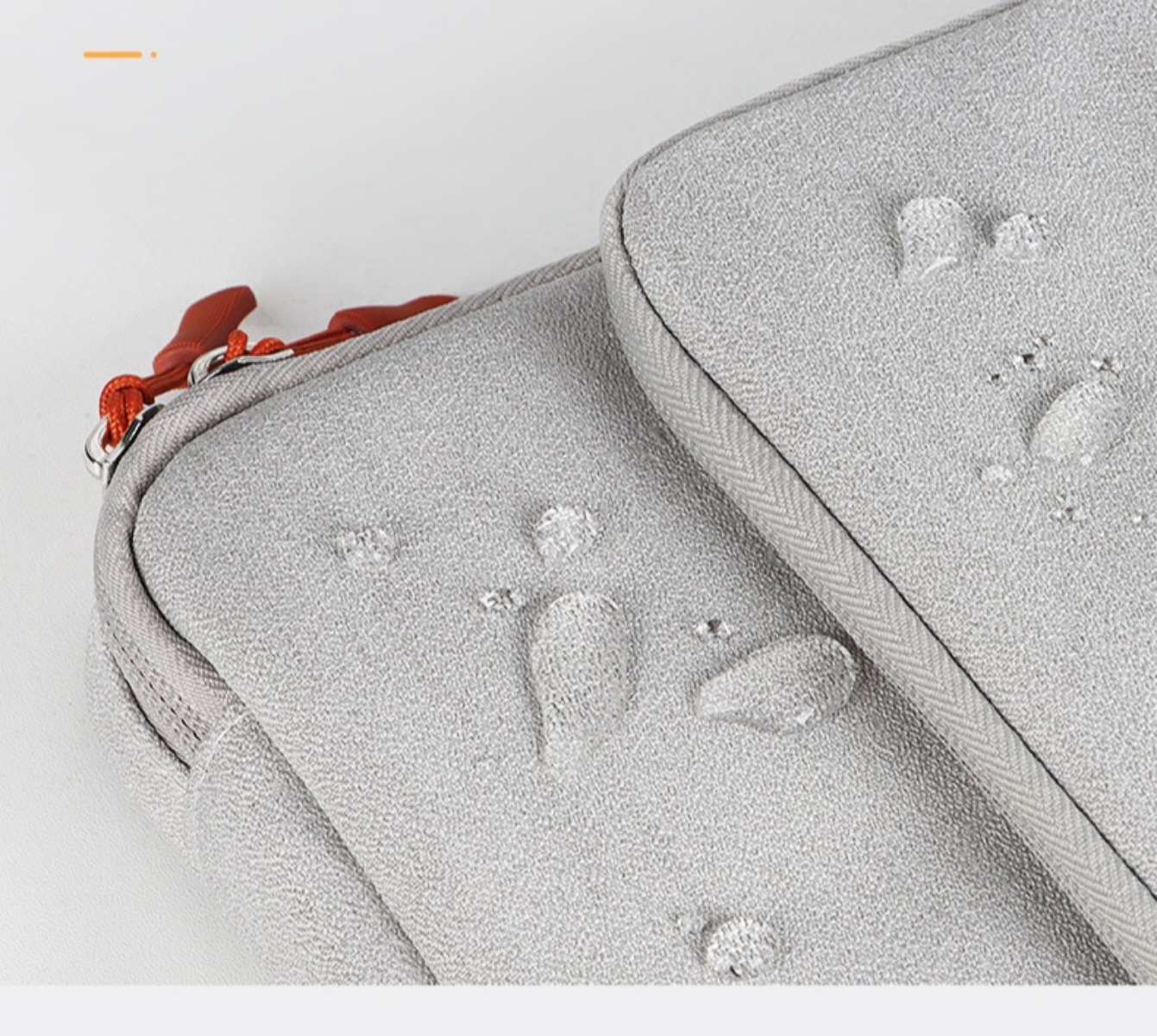 Nahaufnahme einer grauen Laptoptasche mit Wassertropfen auf der Oberfläche, die Wasserbeständigkeit zeigt.