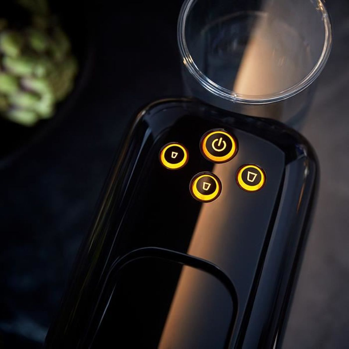 Dispositivo negro con botones y un vaso. Muestra un dispositivo negro con botones iluminados en naranja y un vaso encima.