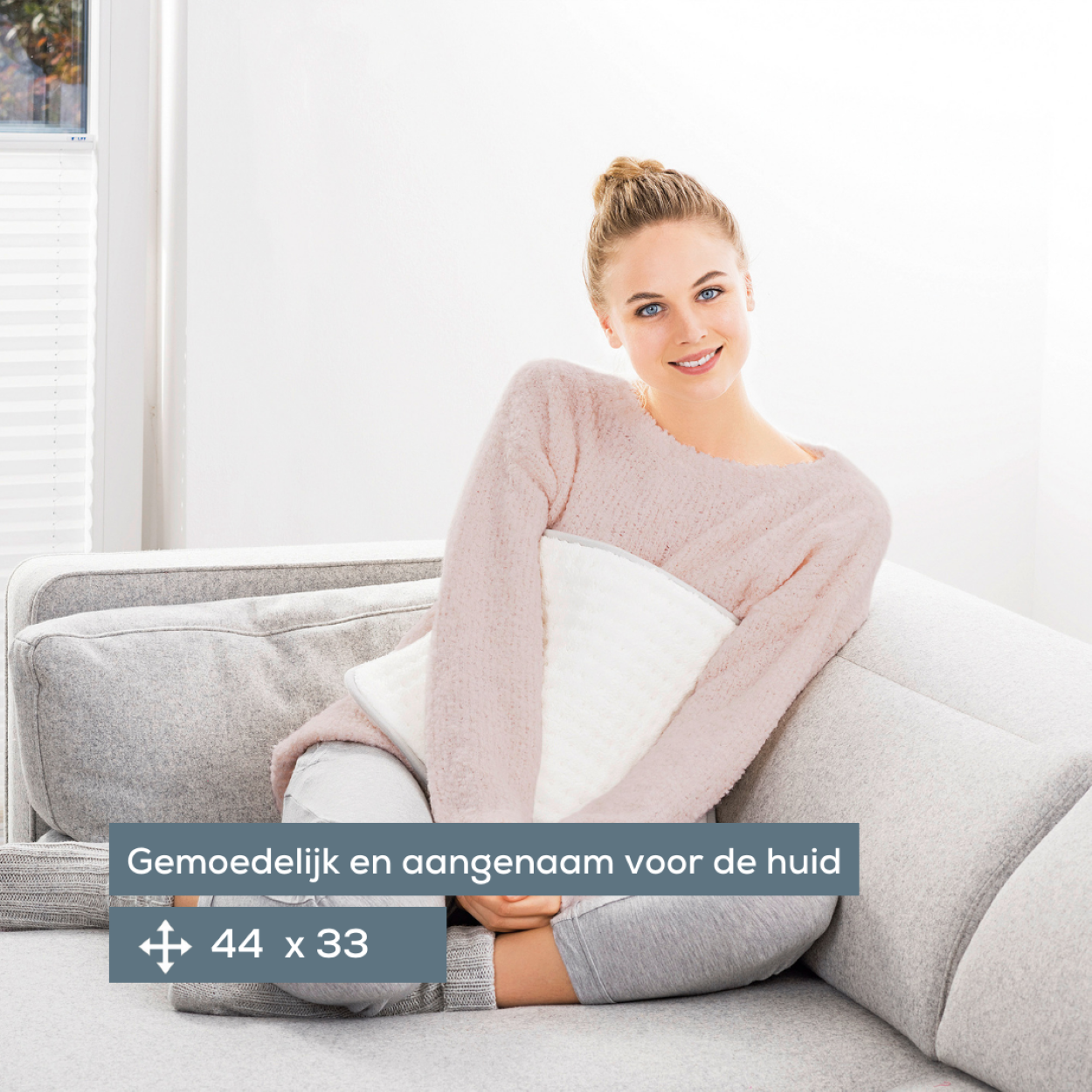 Eine Frau auf einem grauen Sofa hält ein weißes Kissen. Text: 'Angenehm für die Haut'.