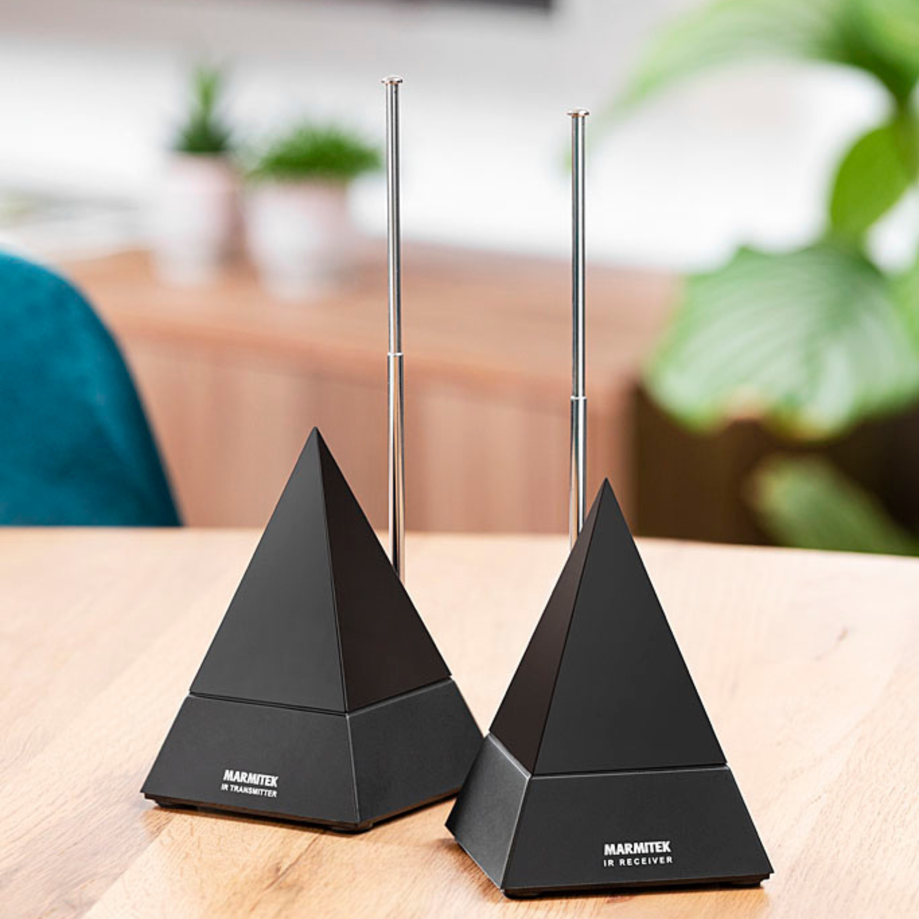 Two black pyramid-shaped devices with antennas on a wooden table. The background is a blurred scene.