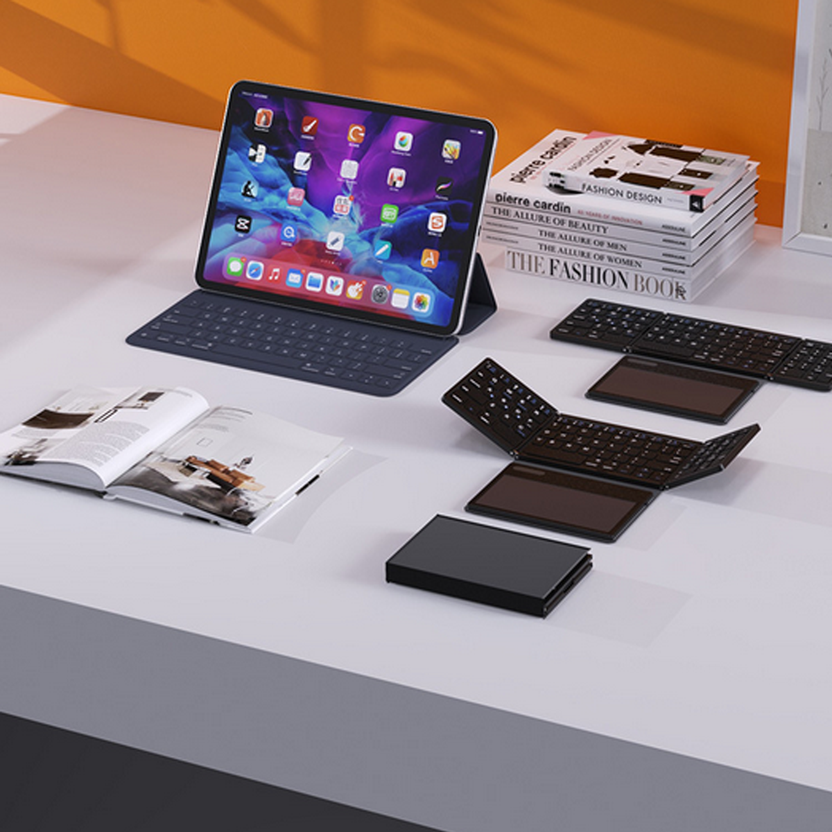 Ein offenes Tablet mit Tastaturhülle und zwei abnehmbaren Tastaturen auf einem weißen Tisch. Bücher sind auch da.