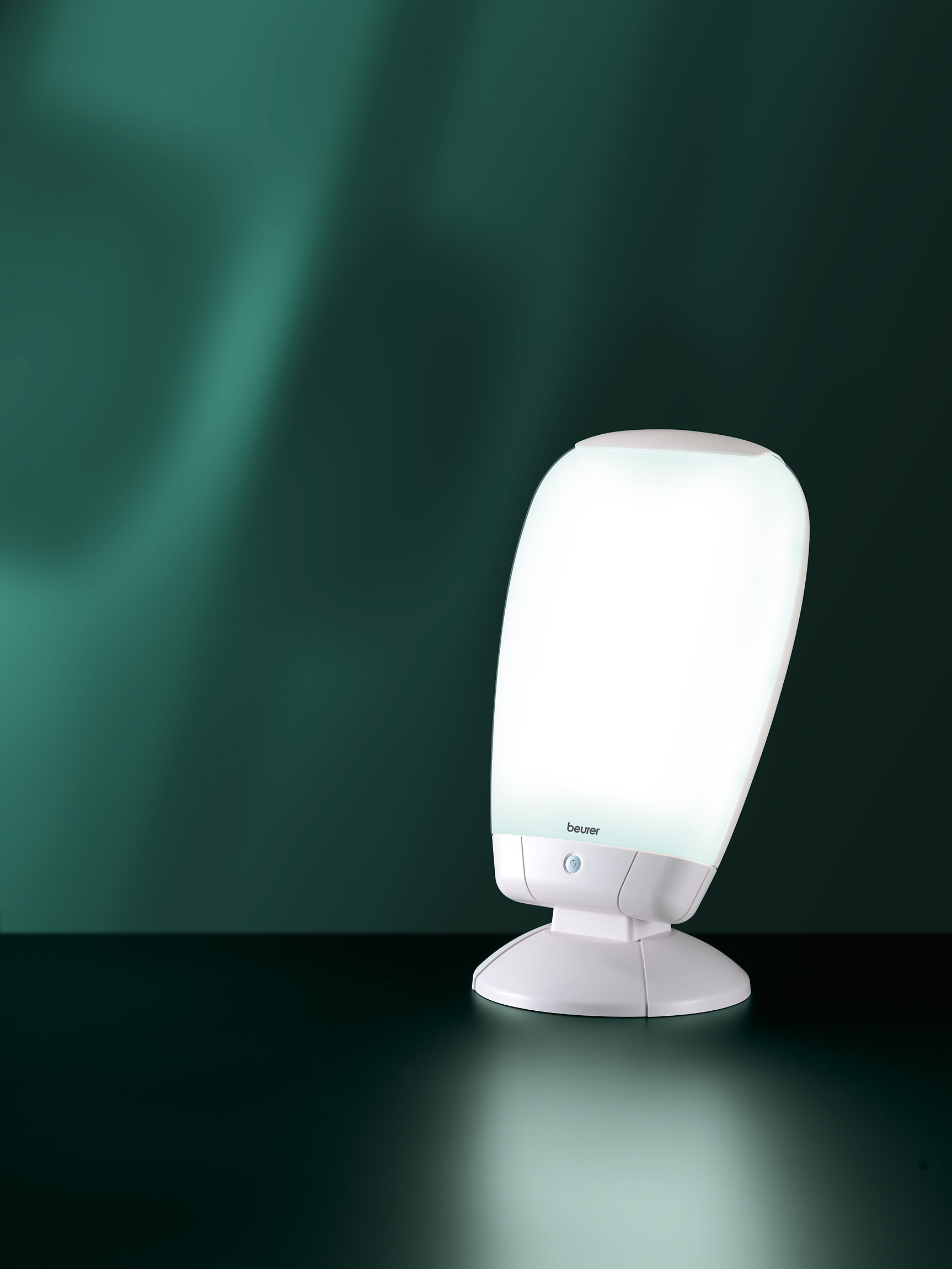 A white, modern, bright-light therapy lamp, angled against a dark green background.