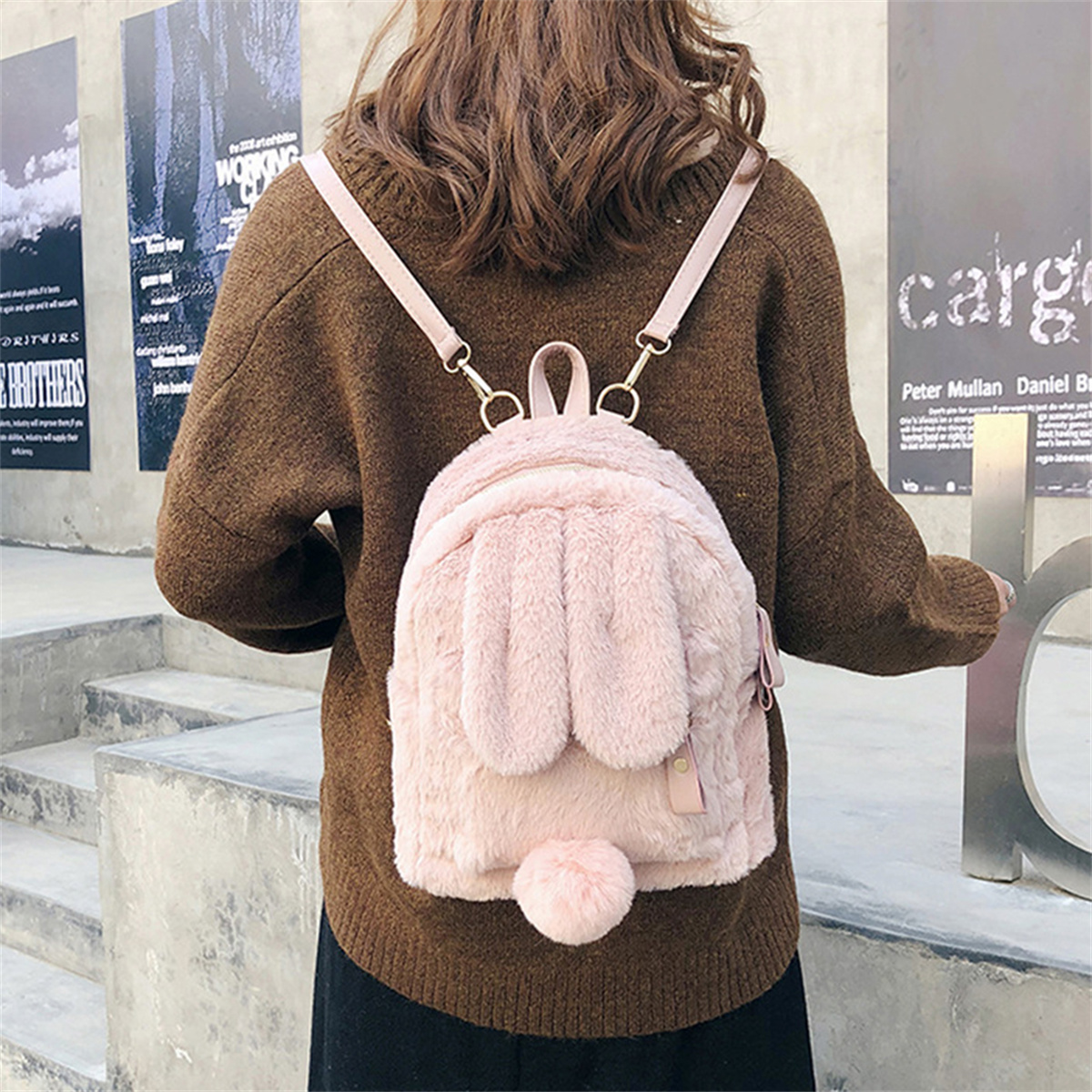 Frau mit braunem Pullover und pinkfarbenem, flauschigem Hasenrucksack, steht mit dem Rücken zur Kamera.