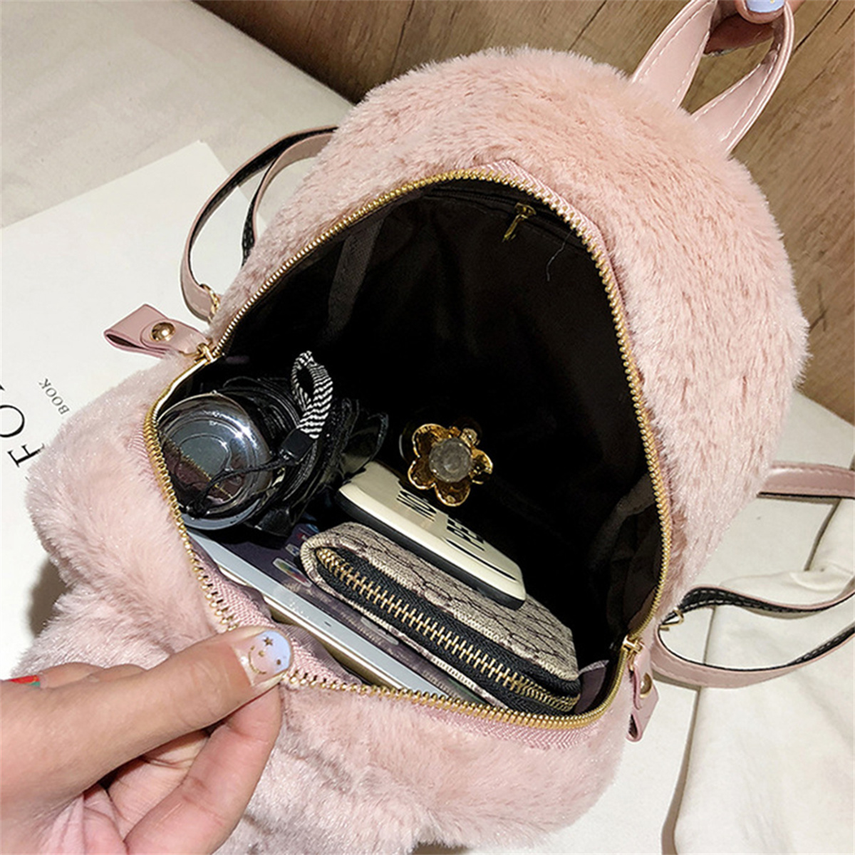 Rosa, flauschiger Rucksack, offen. Inhalt sind Kamera, Telefon, Brieftasche und andere Artikel.