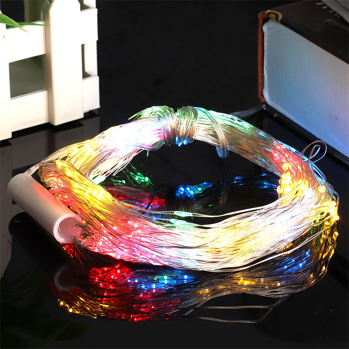 Eine Lichterkette mit mehrfarbigen LEDs, auf schwarzer Oberfläche, mit weißem Akkupack.