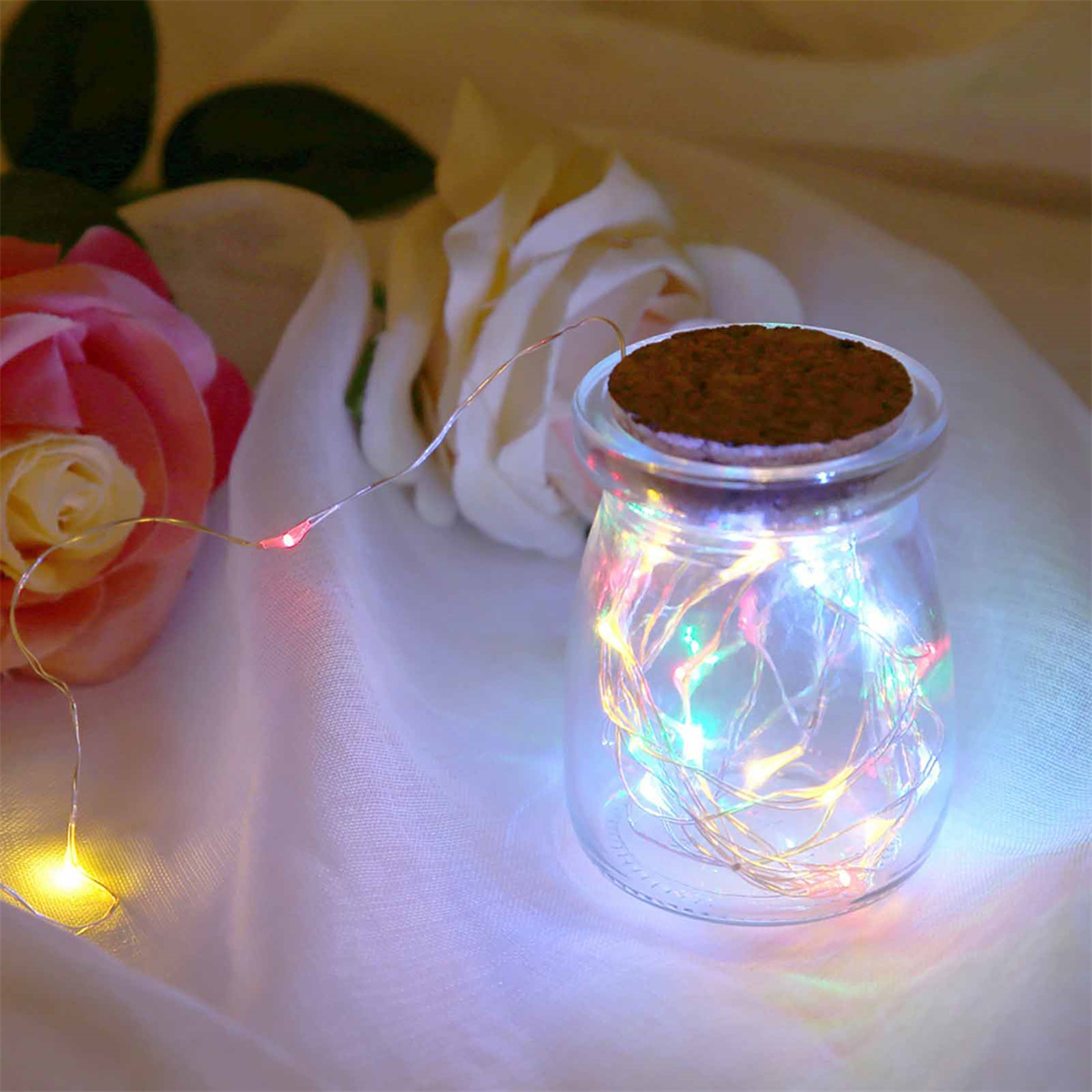 Glasgefäß mit bunten Lichtern und Korkdeckel, mit Blumen im Hintergrund.