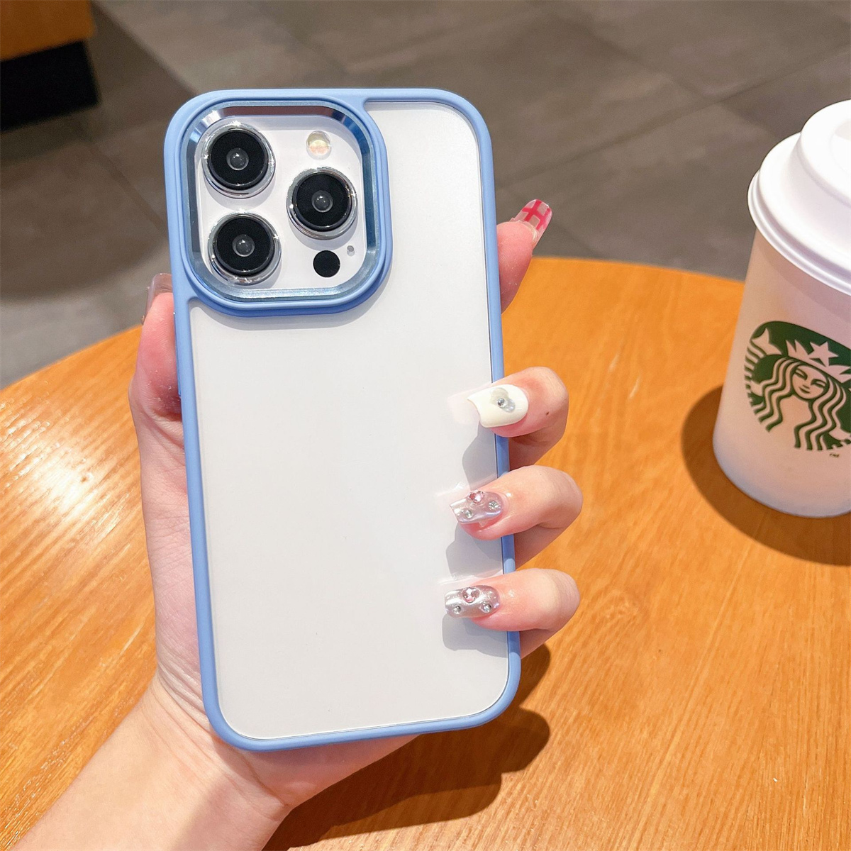Eine Hand, die ein weißes Telefon mit blauem Gehäuse hält. Im Hintergrund ein Starbucks-Becher.