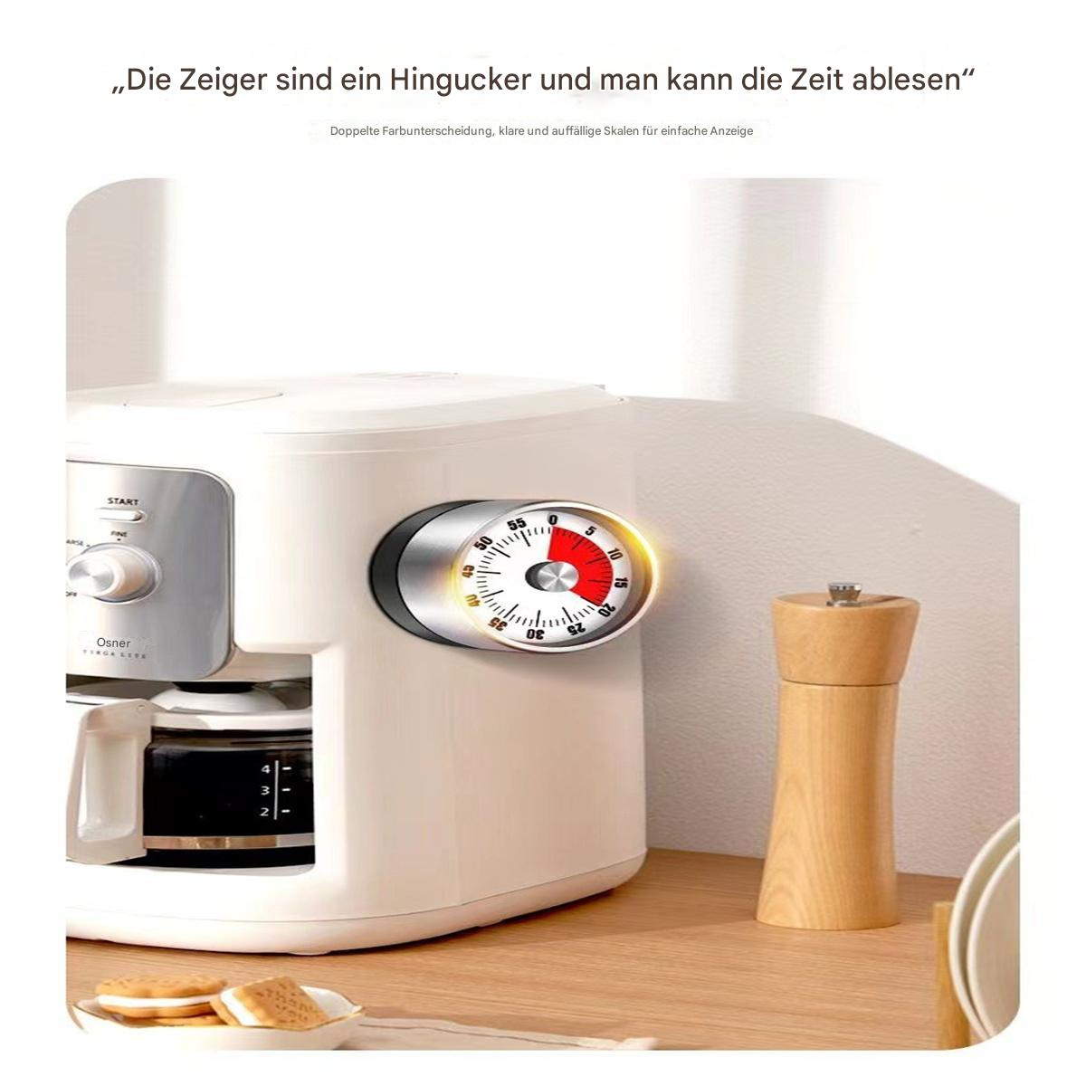 Weiße Kaffeemaschine mit rotem Timer. Ein hölzerner Pfefferstreuer und einige Kekse auf dem Tisch.