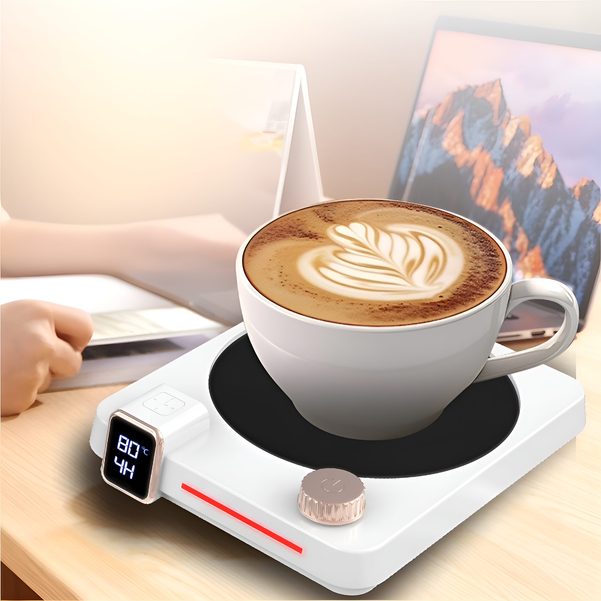 Ein weißer Kaffee-Wärmer mit einer Kaffeetasse darauf. Ein Laptop und eine Hand im Hintergrund.