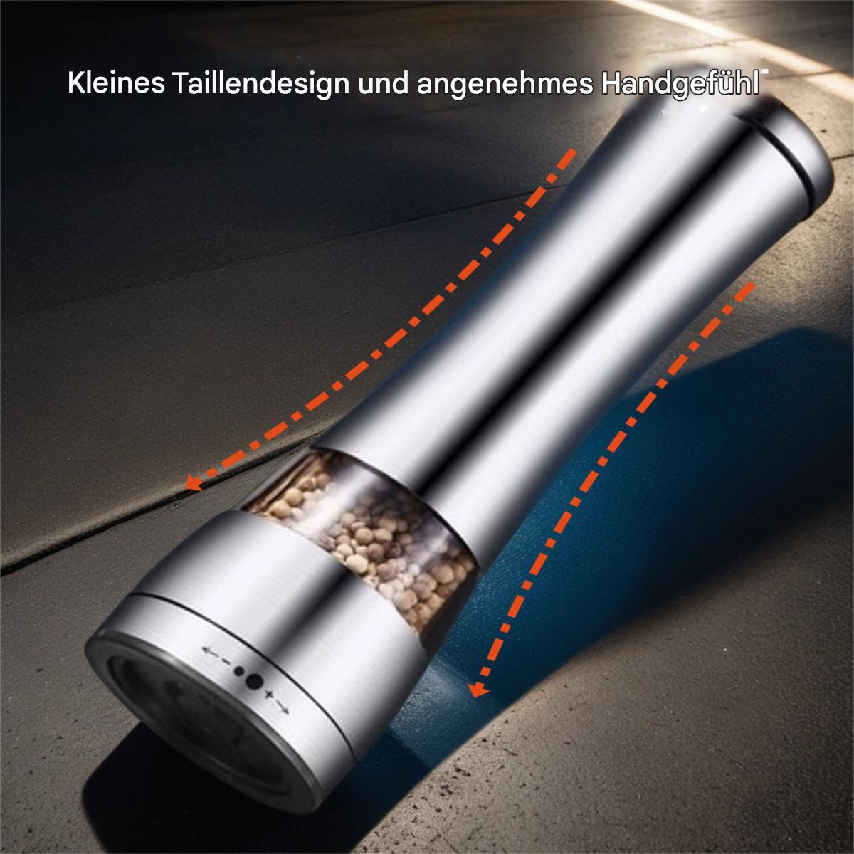 Eine silberne Pfeffermühle mit einem Glasteil, der mit Pfefferkörnern gefüllt ist. Sie steht auf einer dunklen Oberfläche.