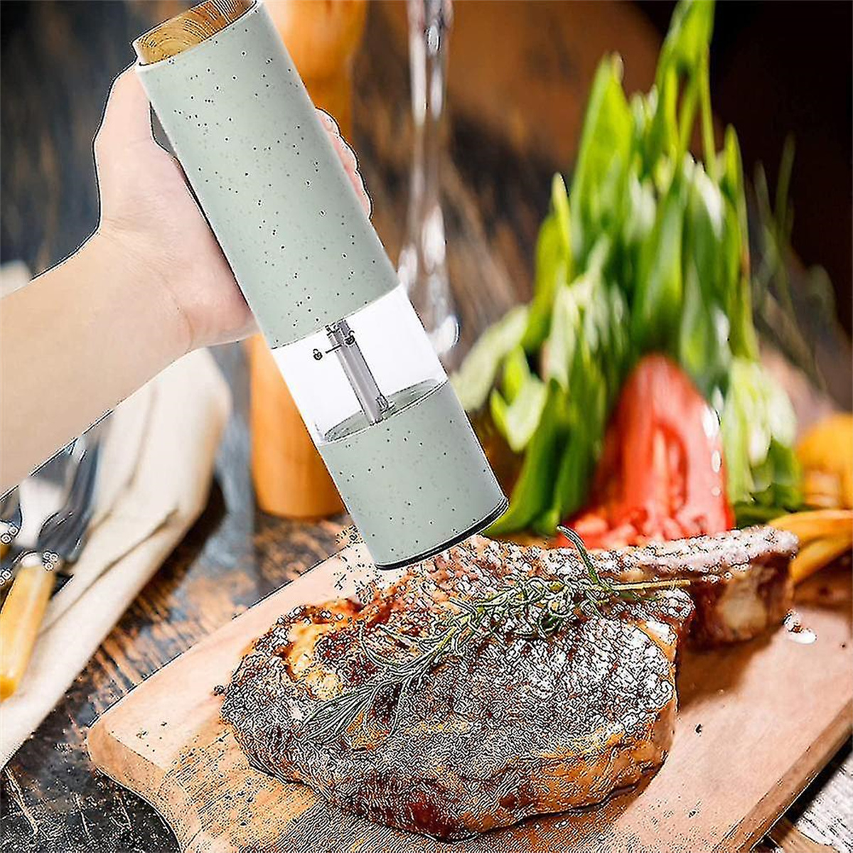 Eine Hand mahlt Pfeffer auf ein Steak auf einem Holzbrett, mit Kräutern auf dem Brett.