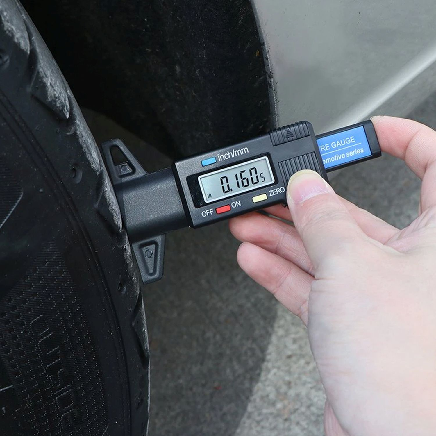 Ein Reifentiefenmesser misst die Profiltiefe und zeigt 0,160 Zoll an. Eine Hand hält das Messgerät in der Nähe eines Autoreifens.