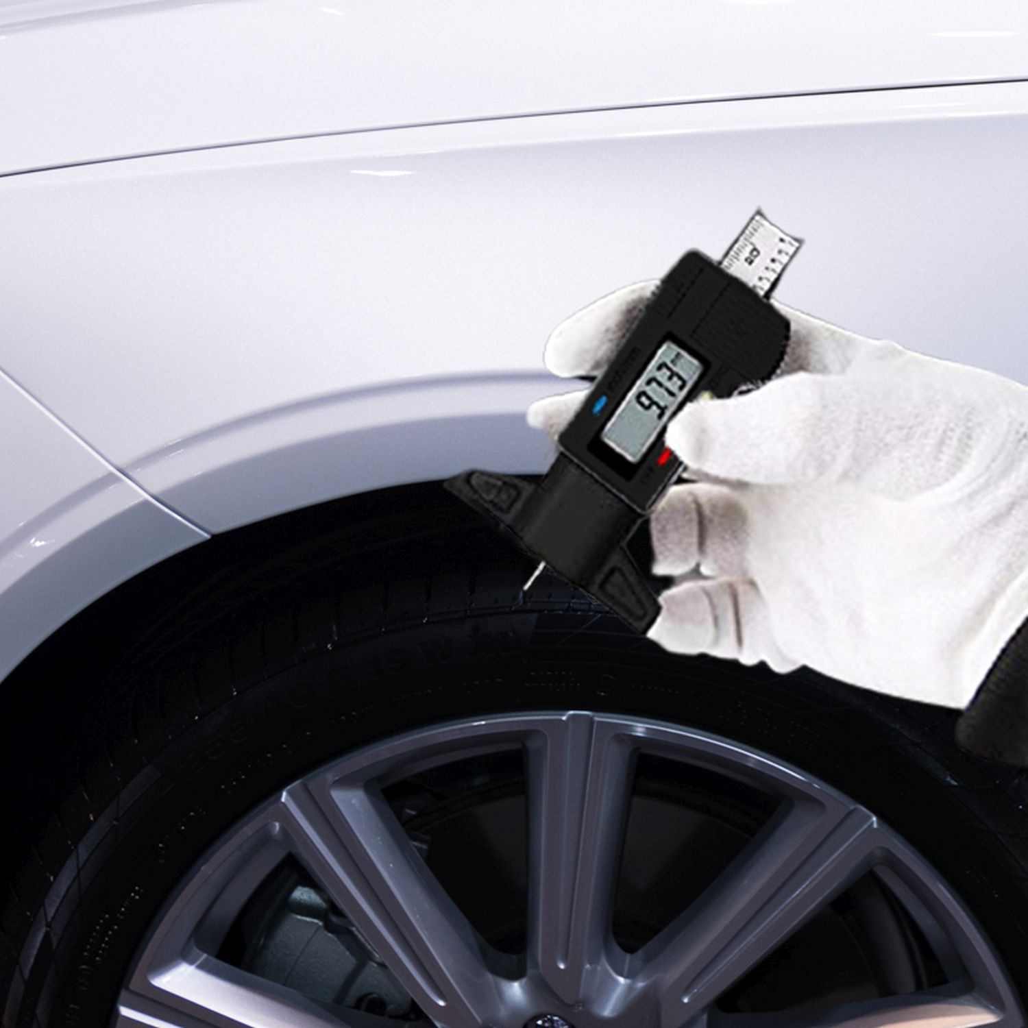 Hand mit weißem Handschuh verwendet ein digitales Profiltiefenmessgerät an einem Autoreifen, das einen Wert anzeigt.